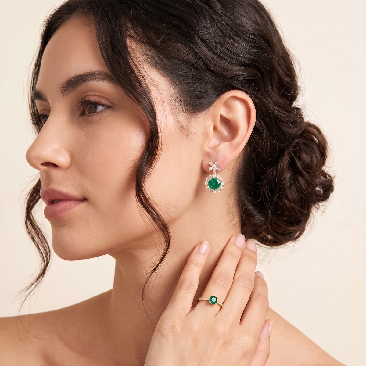 A model is wearing The Antoinette Round Emerald & Diamond Halo Pendant Earrings with Flower Bail