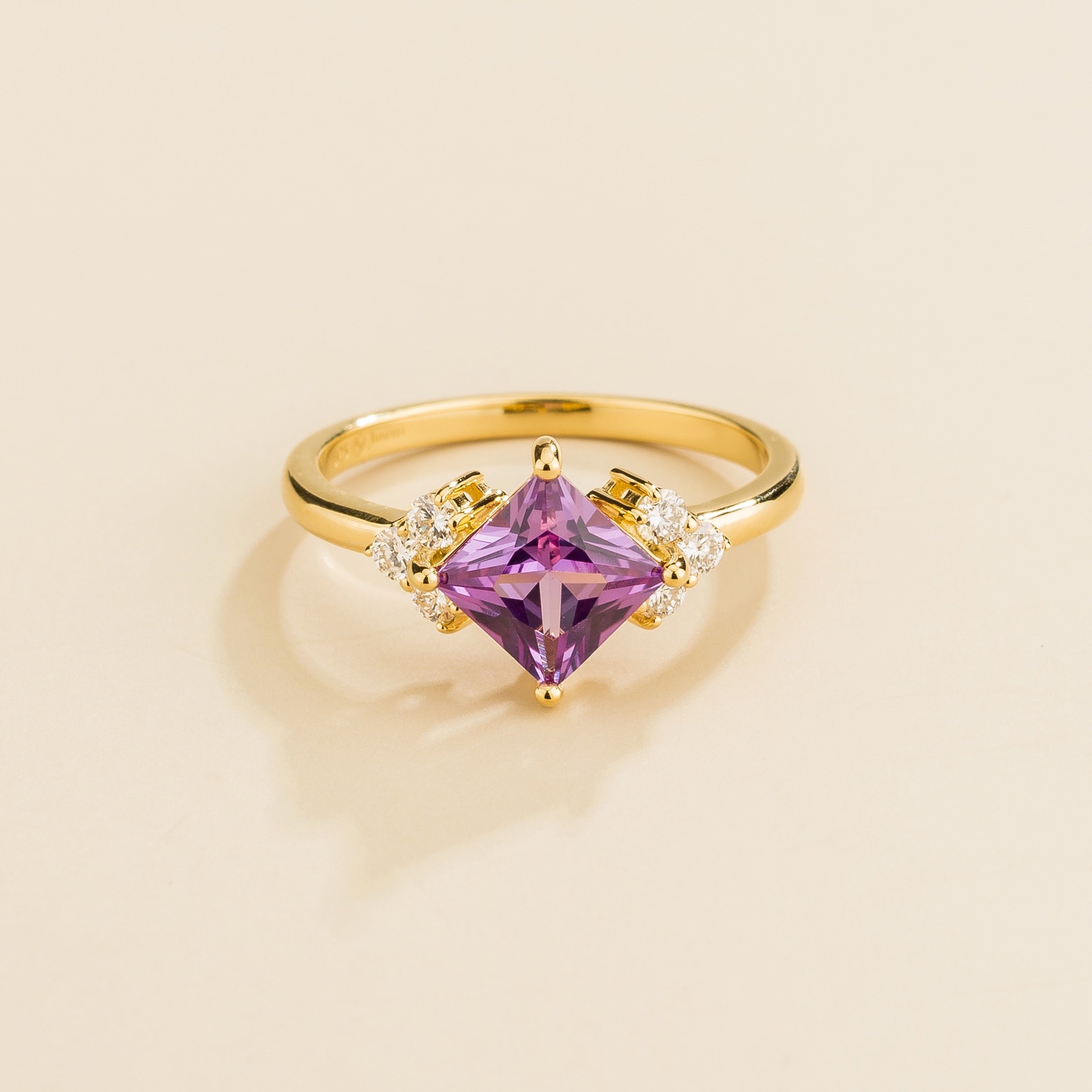 A gold ring with a princess-cut purple sapphire center stone and smaller diamond accents on the band.