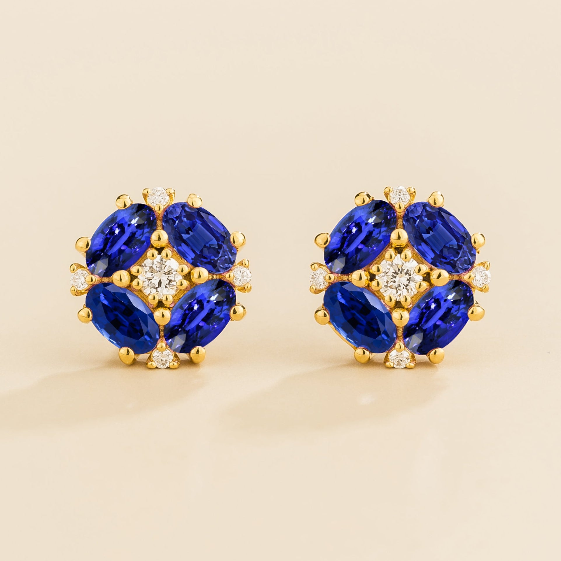 A pair of gold earrings featuring a central round diamond with oval blue sapphire petals arranged around it.
