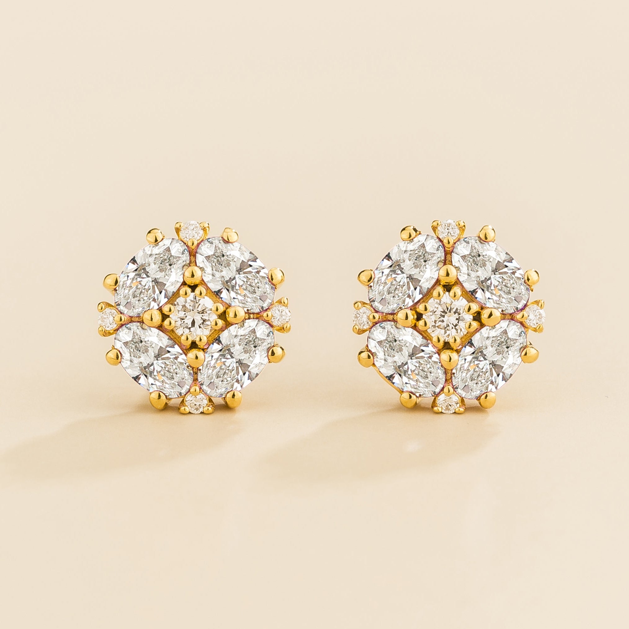 A pair of gold earrings featuring round diamonds cluster with oval diamond petals.