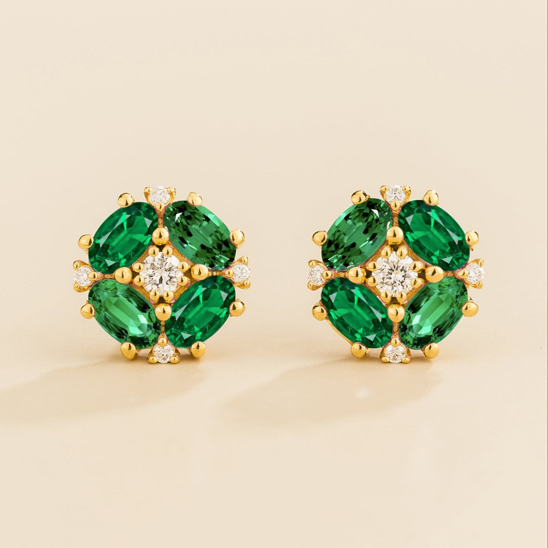 A pair of gold earrings featuring oval green emeralds and round diamonds arranged in a floral pattern.