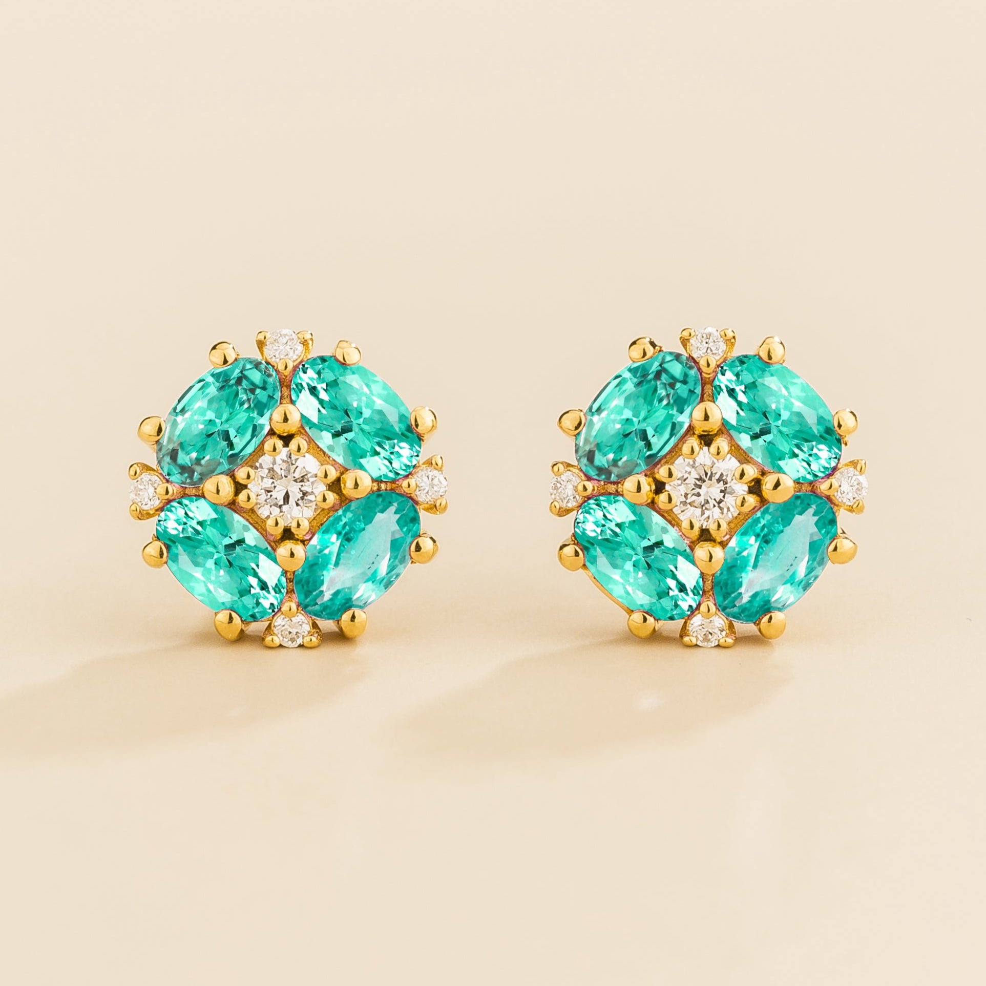 A pair of gold earrings featuring oval paraiba sapphires and round diamonds arranged in a floral pattern.
