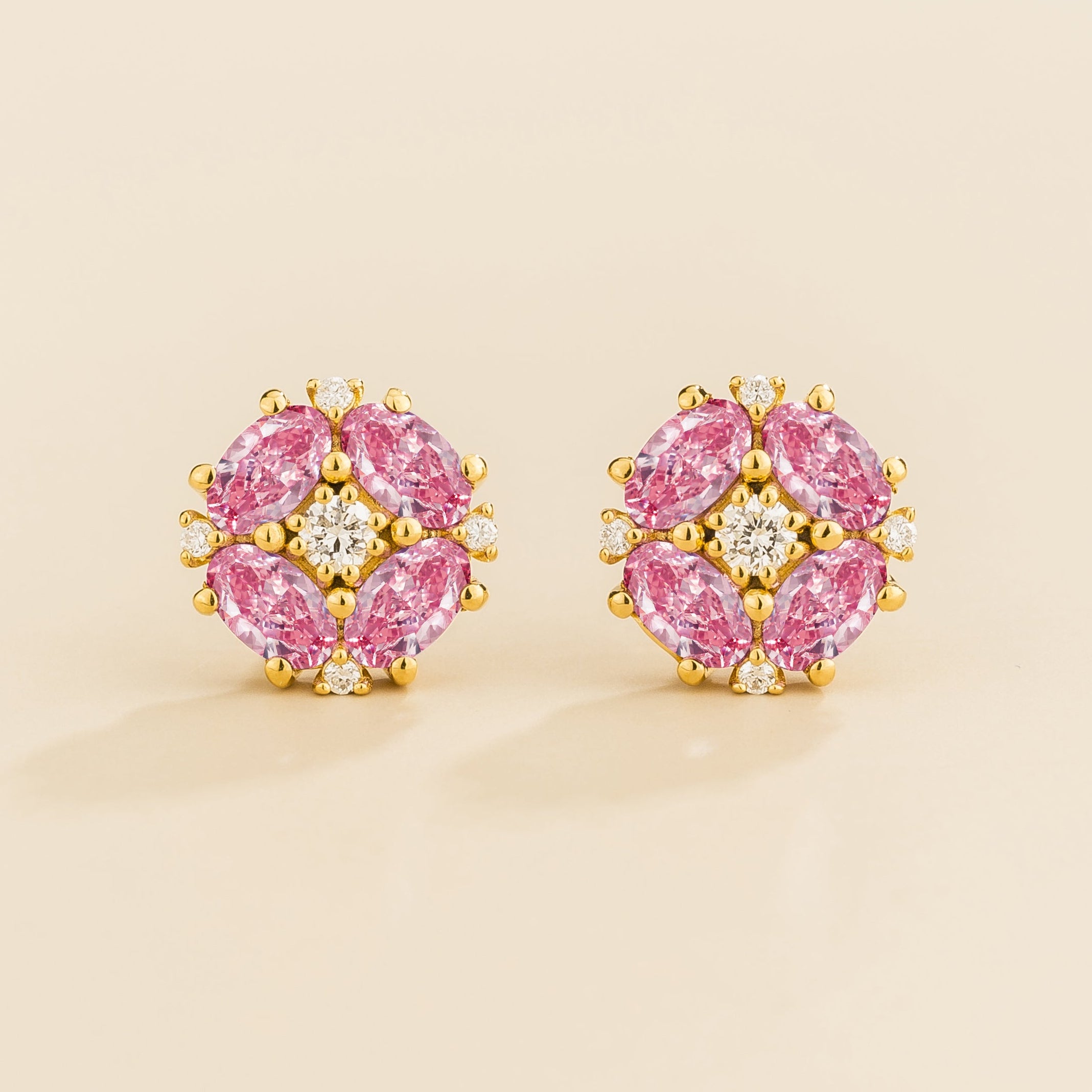 A pair of gold earrings featuring a central round diamond with oval pink sapphire petals arranged around it.