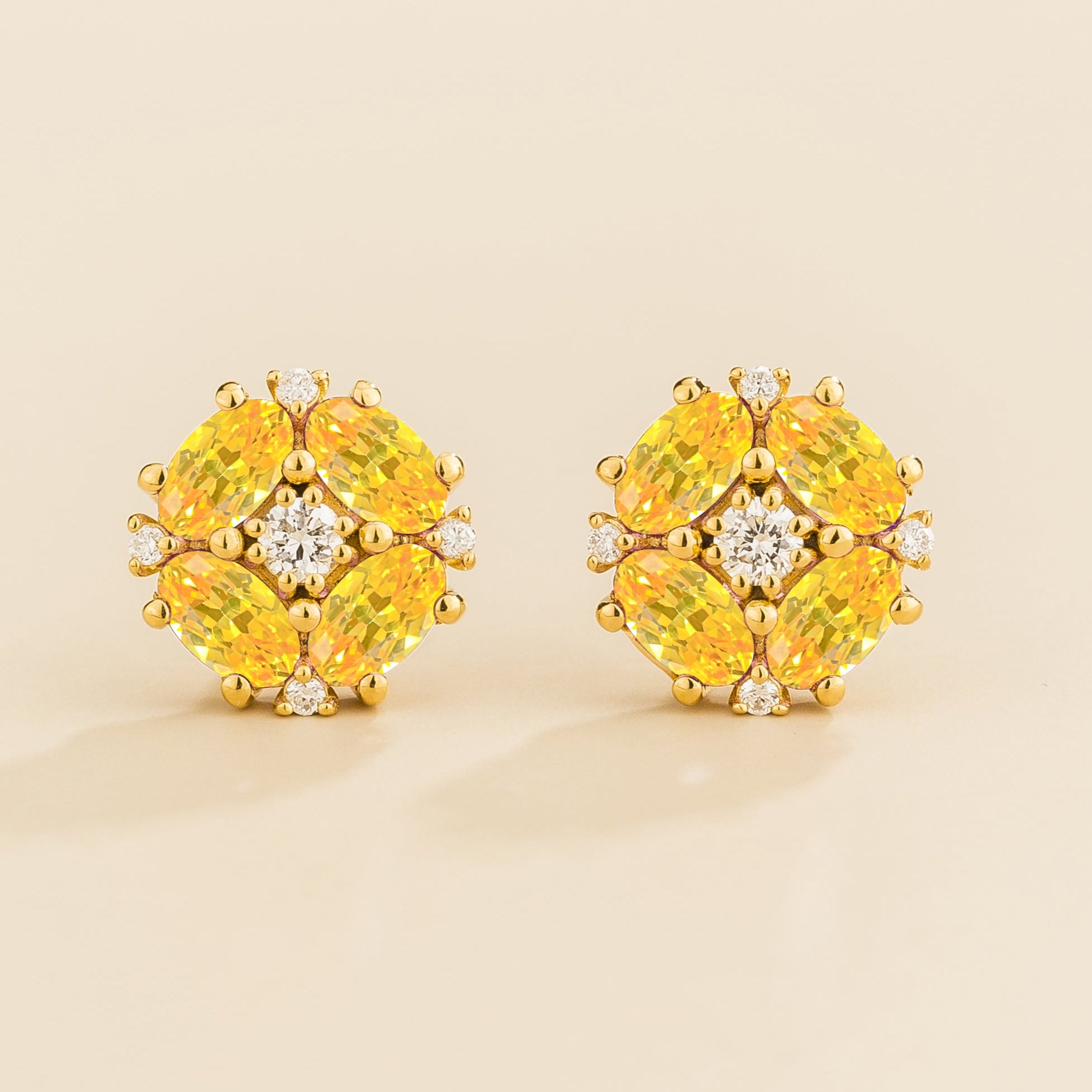 A pair of gold earrings featuring oval yellow sapphire and round diamonds arranged in a floral pattern.