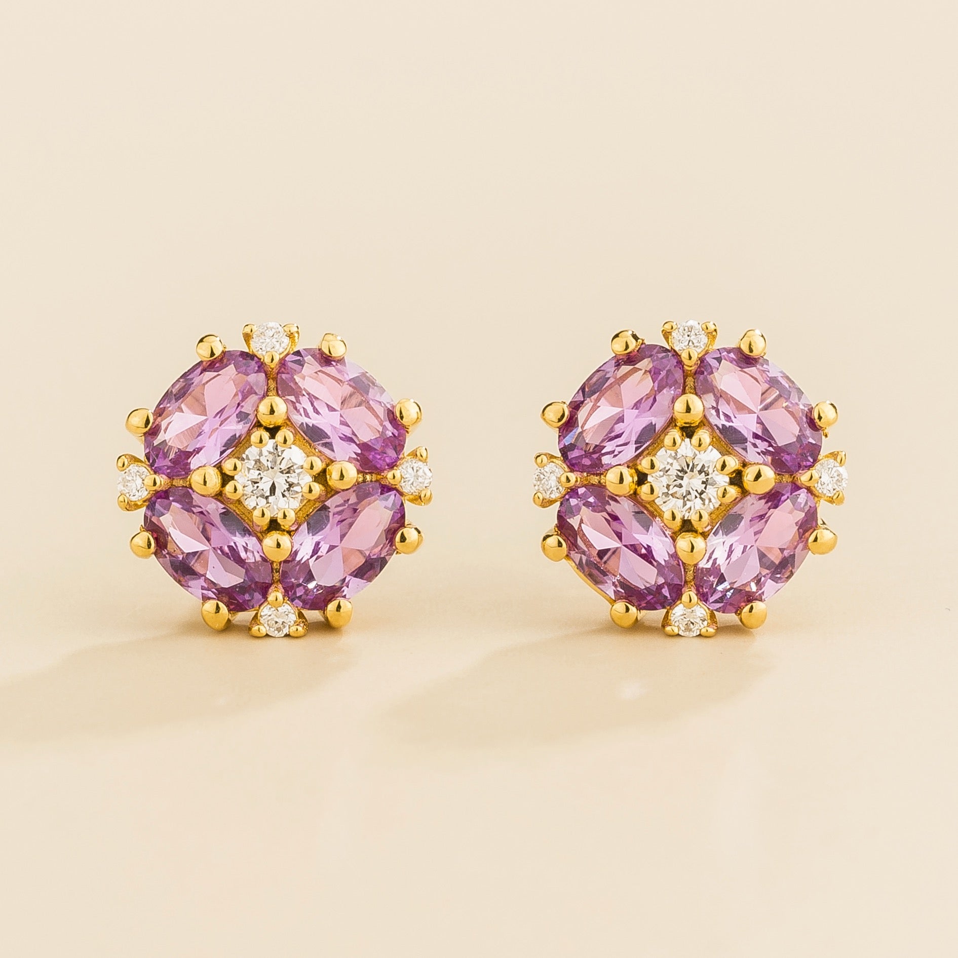 A pair of gold earrings featuring oval purple sapphires and round diamonds arranged in a floral pattern.