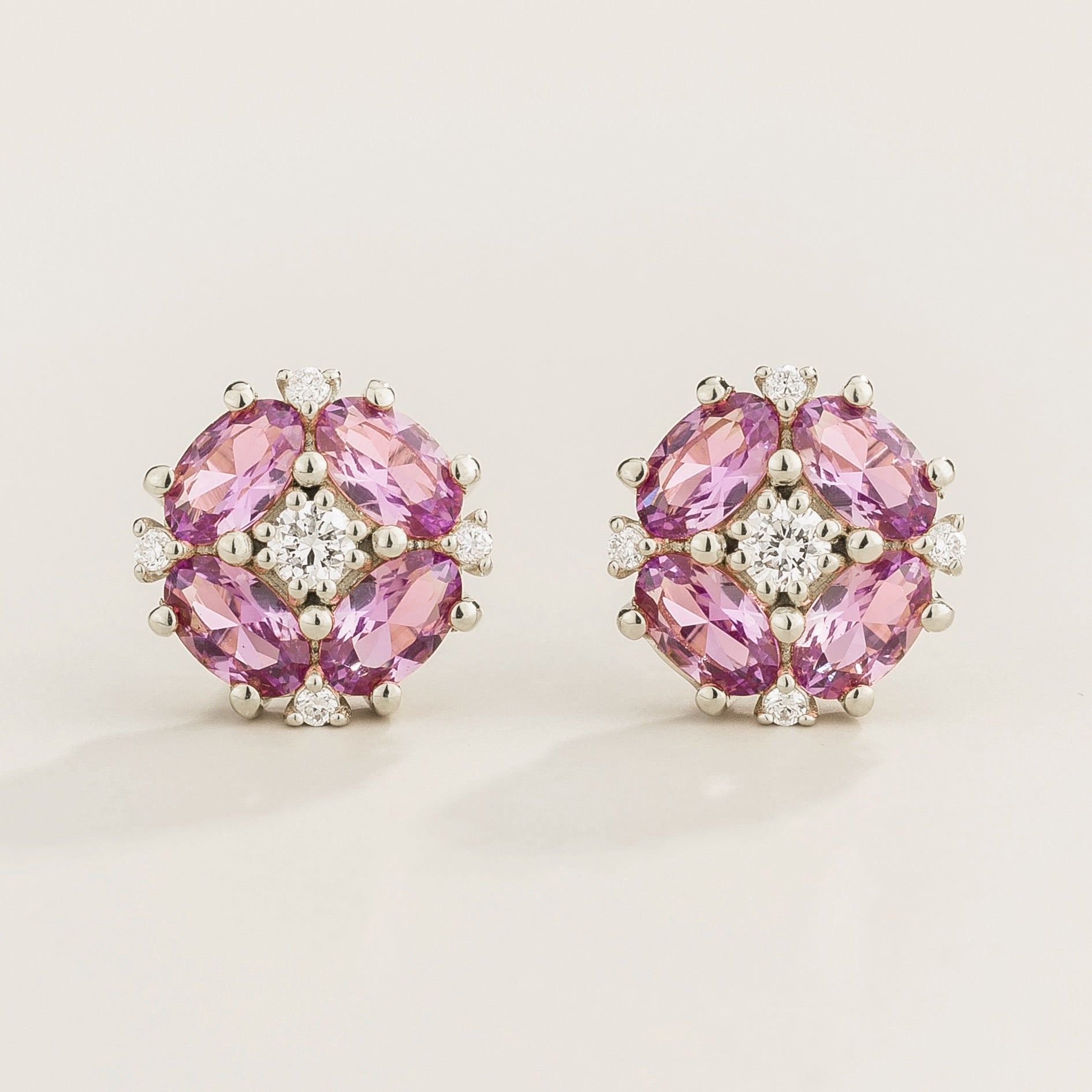 A pair of white gold earrings featuring a central round diamond with oval purple sapphire petals arranged around it.