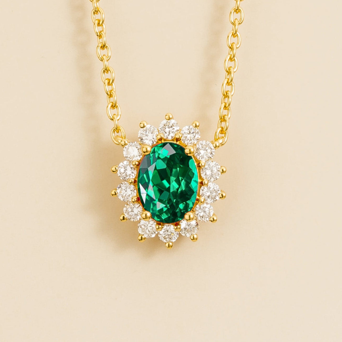 A gold necklace with a central oval-cut emerald surrounded by a halo of round-cut diamonds, displayed against a beige background.