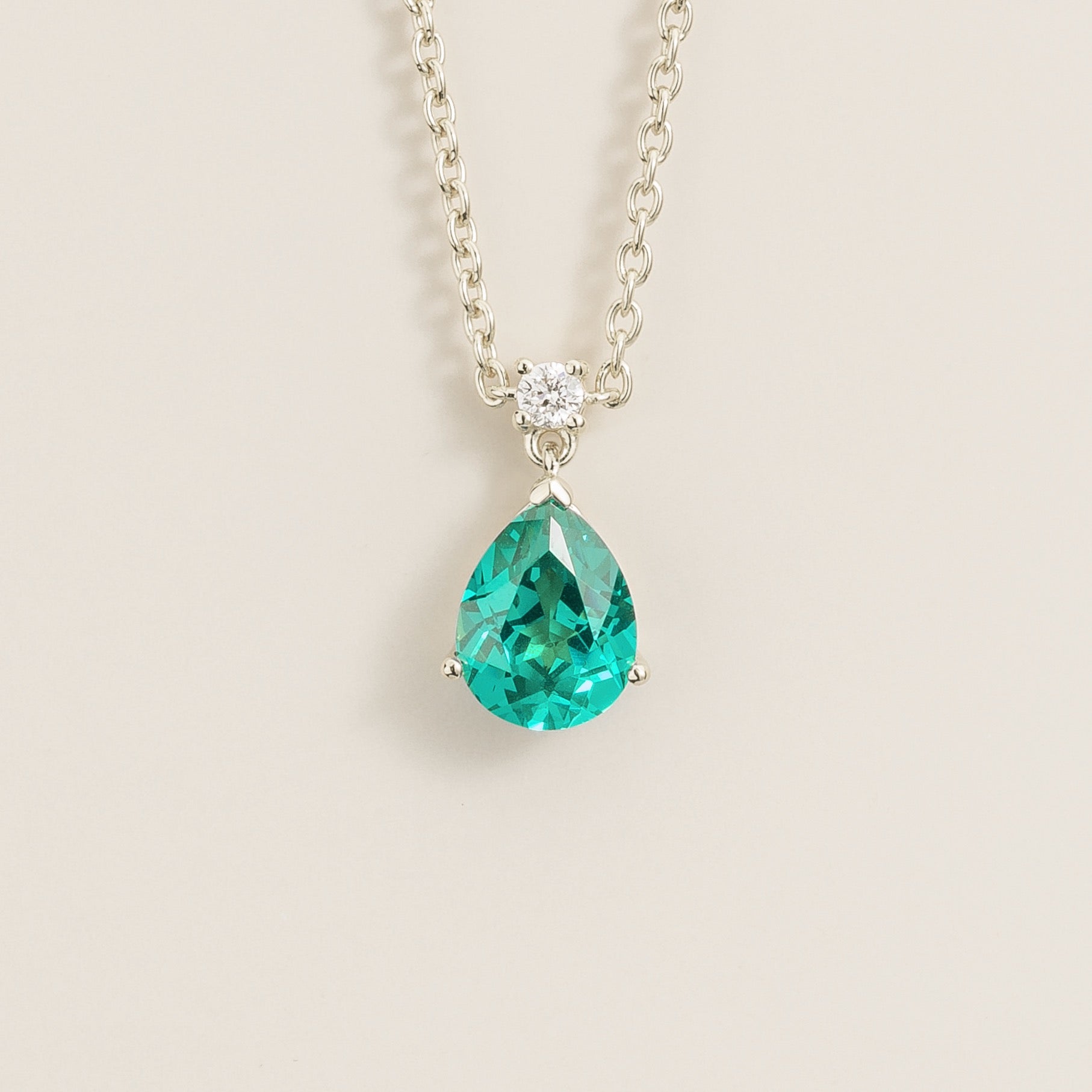 A medium-sized classic pendant necklace in white gold, featuring a pear shape paraiba sapphire centerpiece and smaller round diamonds, displayed against a neutral background.