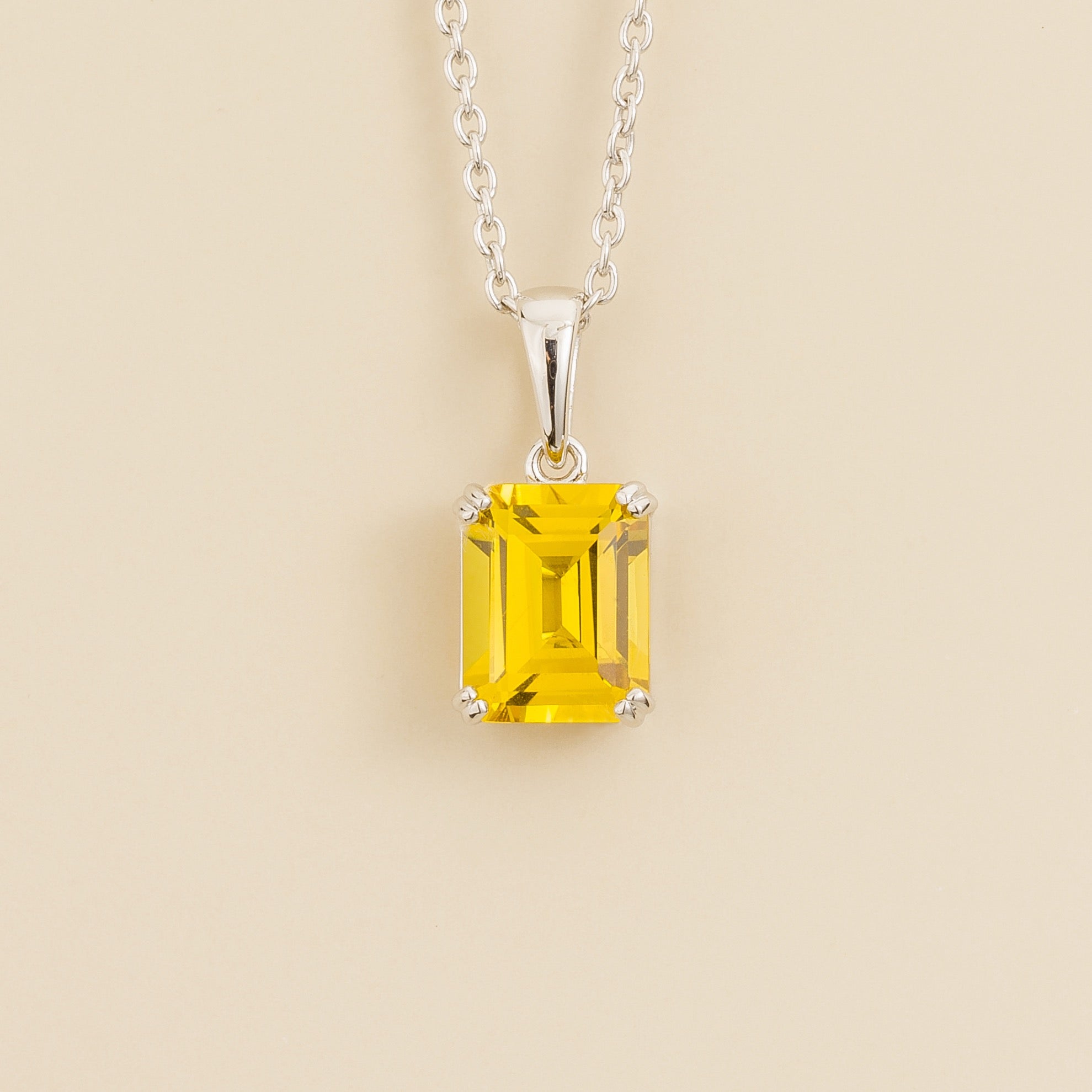 A white gold pendant necklace with an emerald-cut yellow sapphire centerpiece. London jewellery store