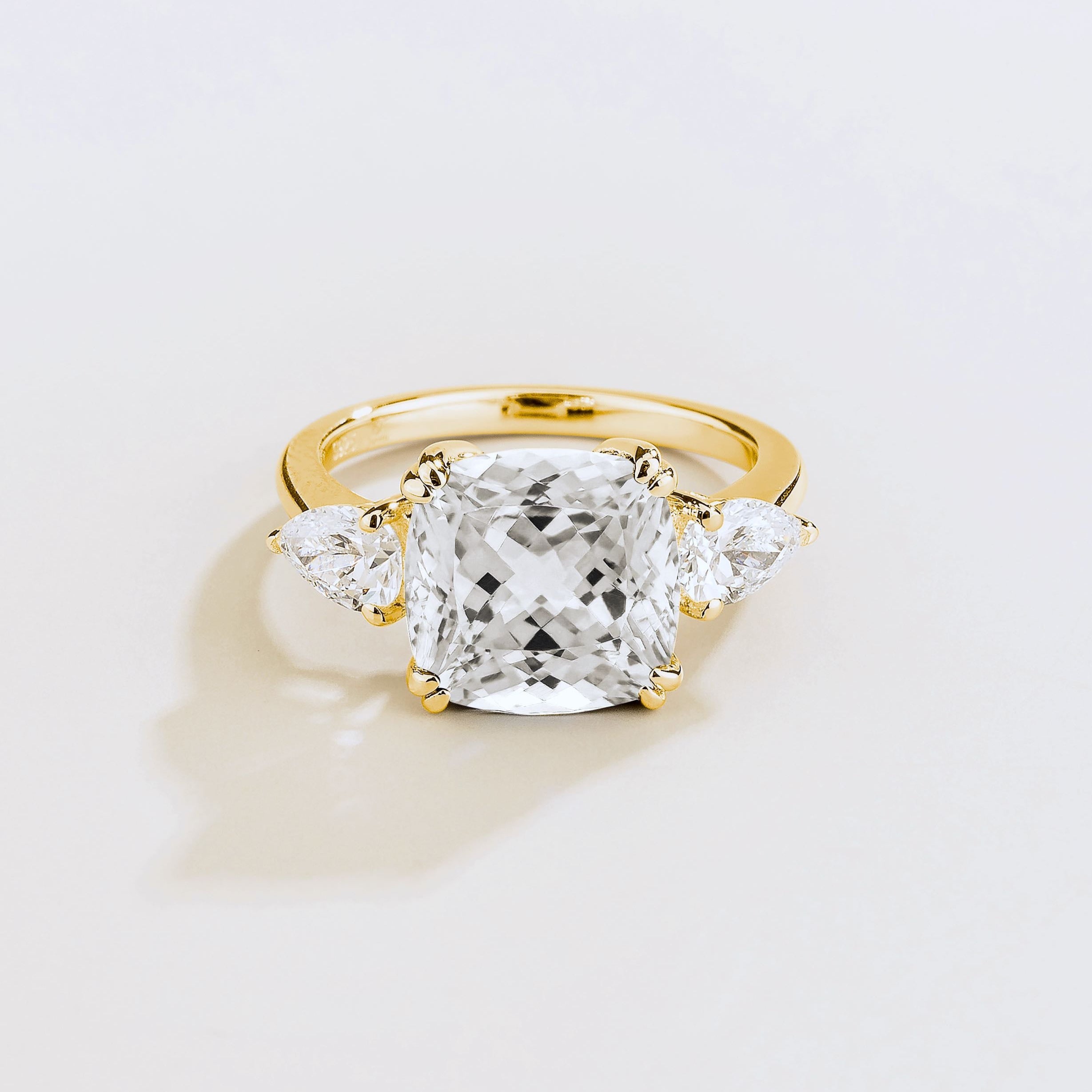 Gold ring with large cushion cut diamond gemstone and pear side diamonds on a beige background