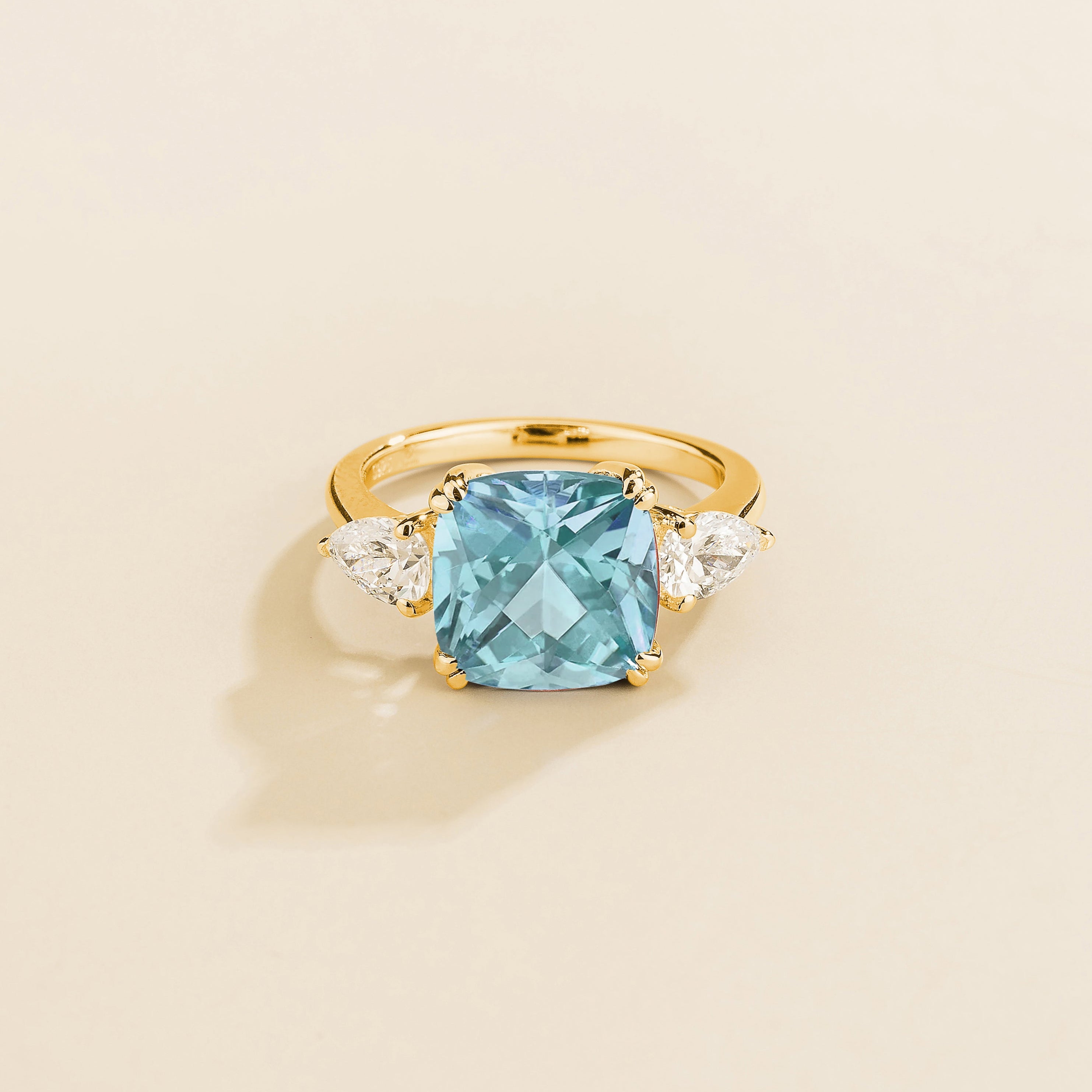 A gold ring with a large aquamarine cushion-cut centerpiece and smaller pear-cut diamond accents on the sides.