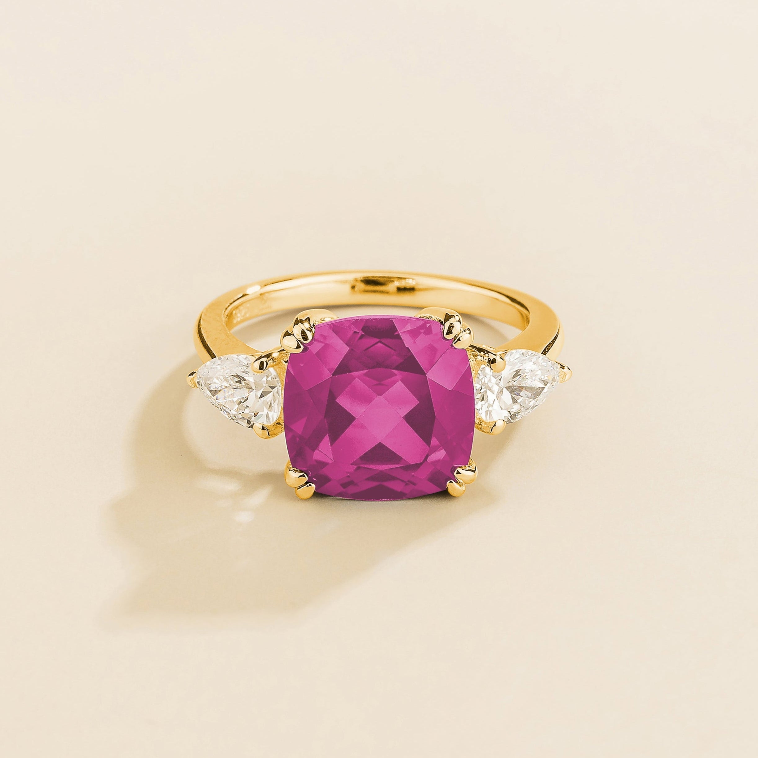 A gold ring with a large vivid pink cushion-cut sapphire centerpiece and smaller pear-cut diamond accents on the sides.