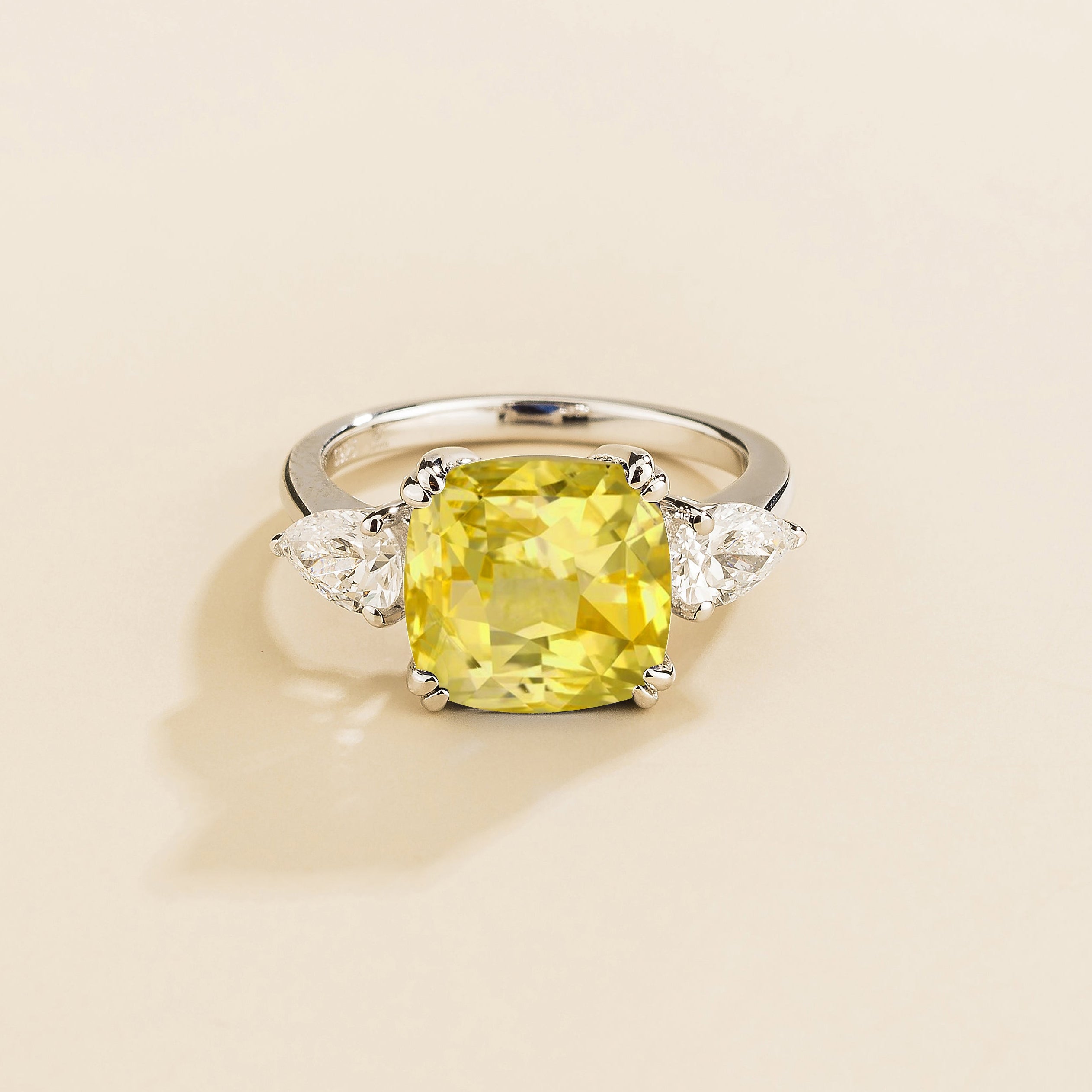 Gold ring with cushion cut yellow sapphire gemstone and pear side diamonds on a beige background