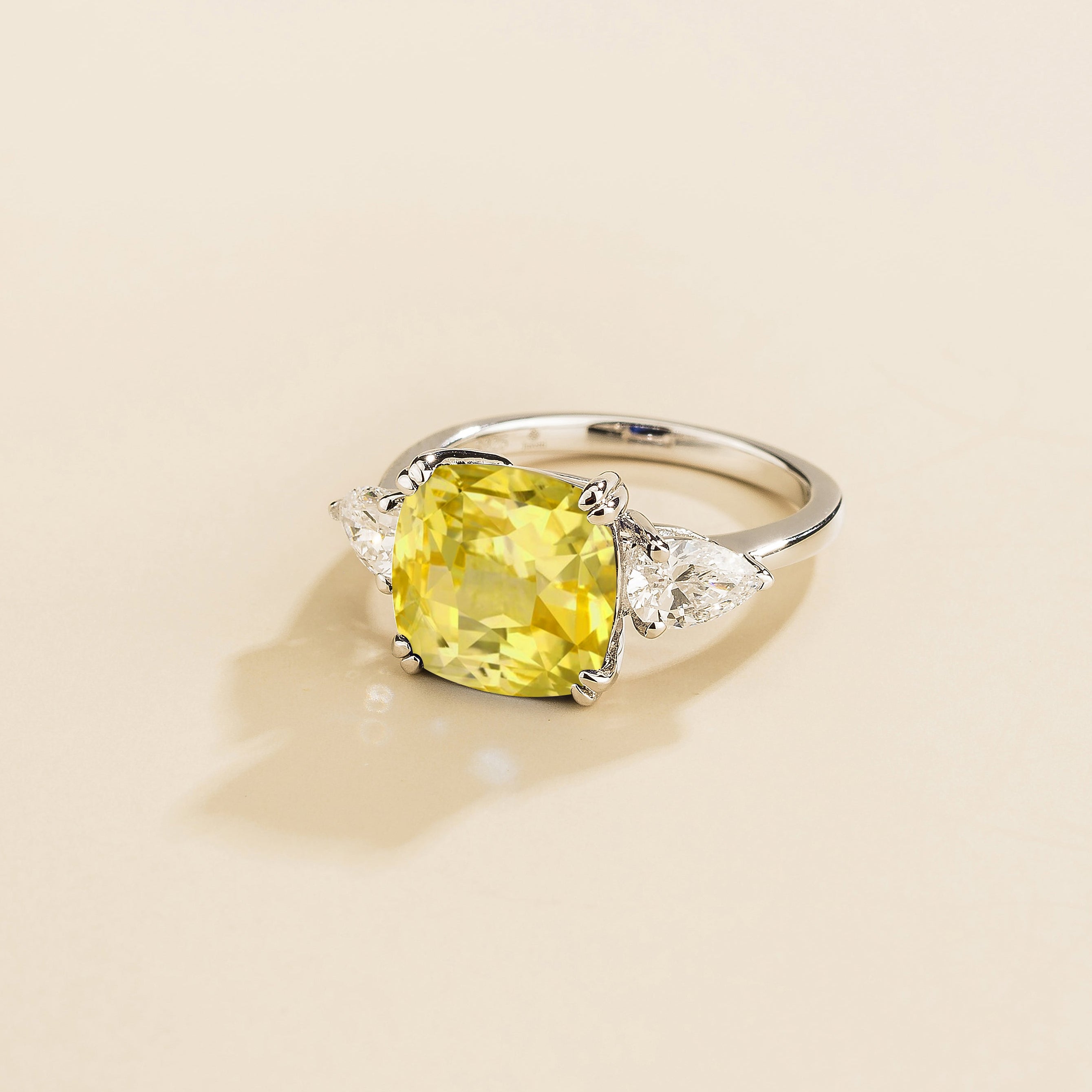 Gold ring with cushion cut yellow sapphire gemstone and pear side diamonds on a beige background