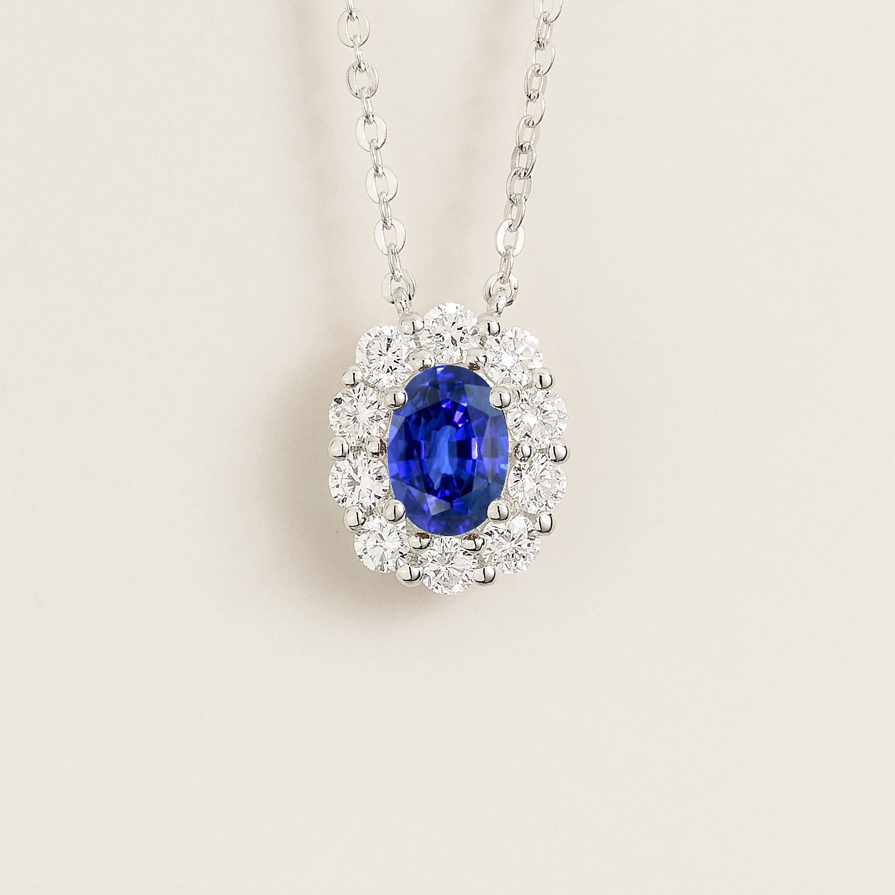 Necklace with an oval blue sapphire gemstone and diamond halo on a light background - Juvetti London