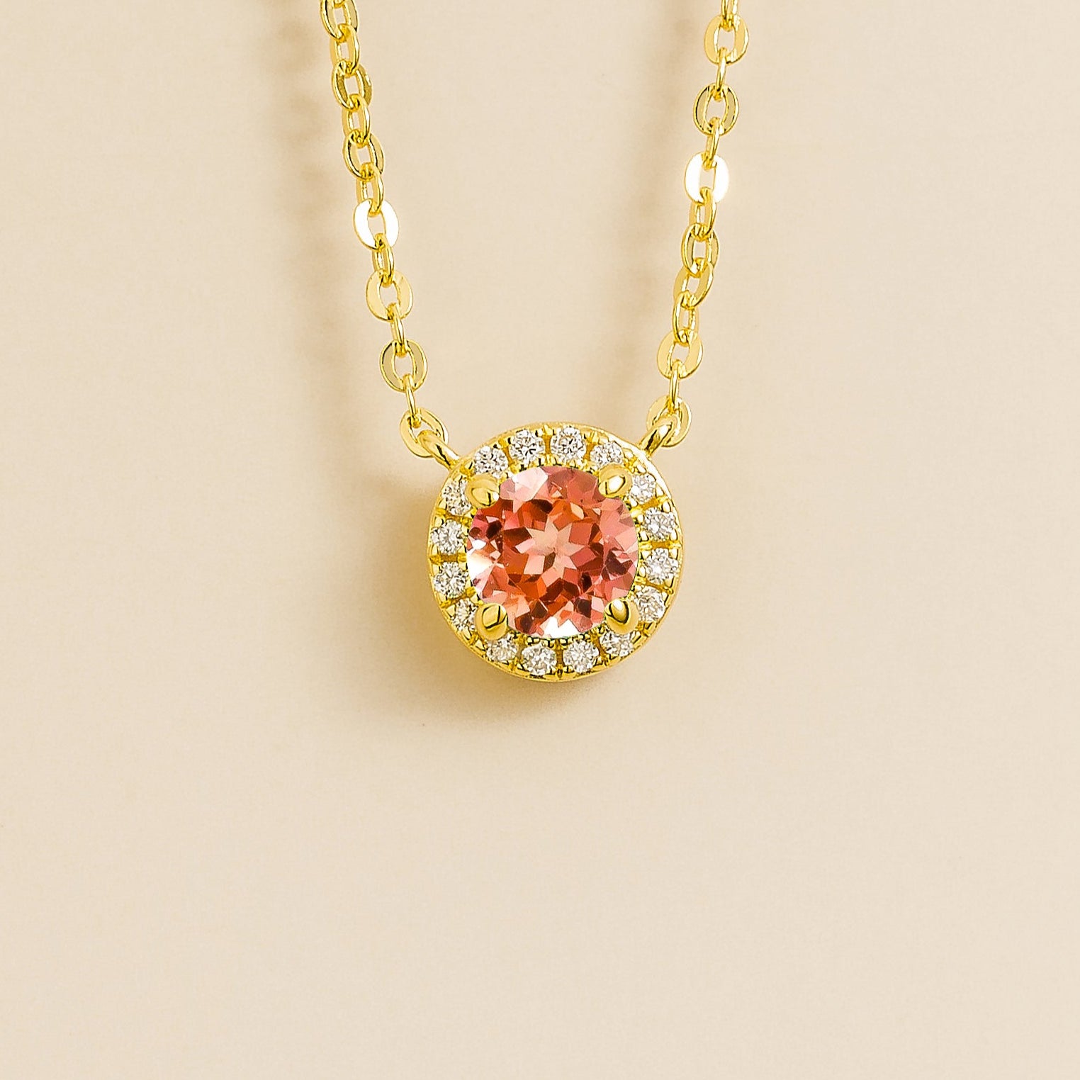 A gold necklace with a halo design featuring a round padparadscha centerpiece surrounded by smaller diamonds, displayed against a light background.