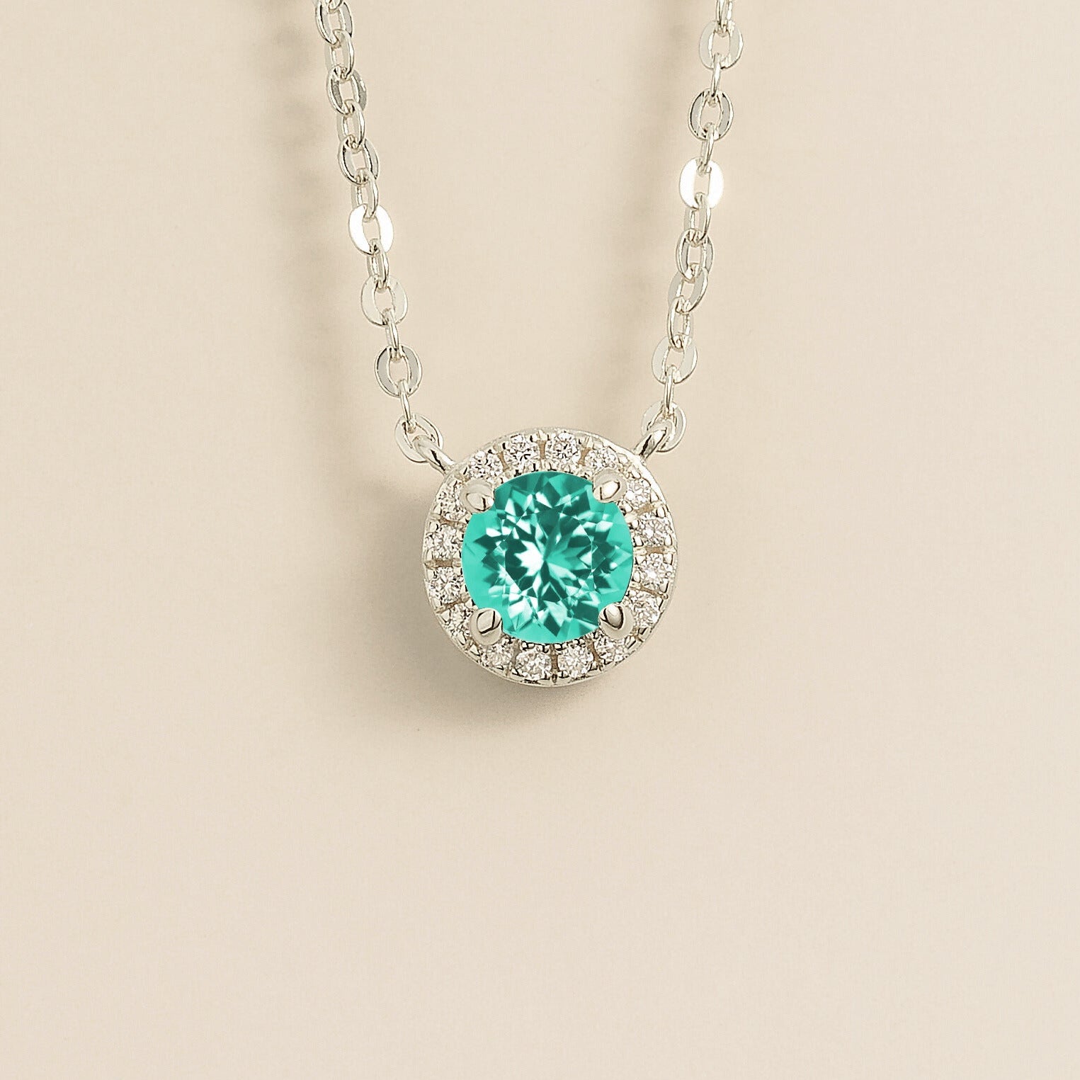 A white gold gold necklace with a halo design featuring a round paraiba centerpiece surrounded by smaller diamonds, displayed against a light background.