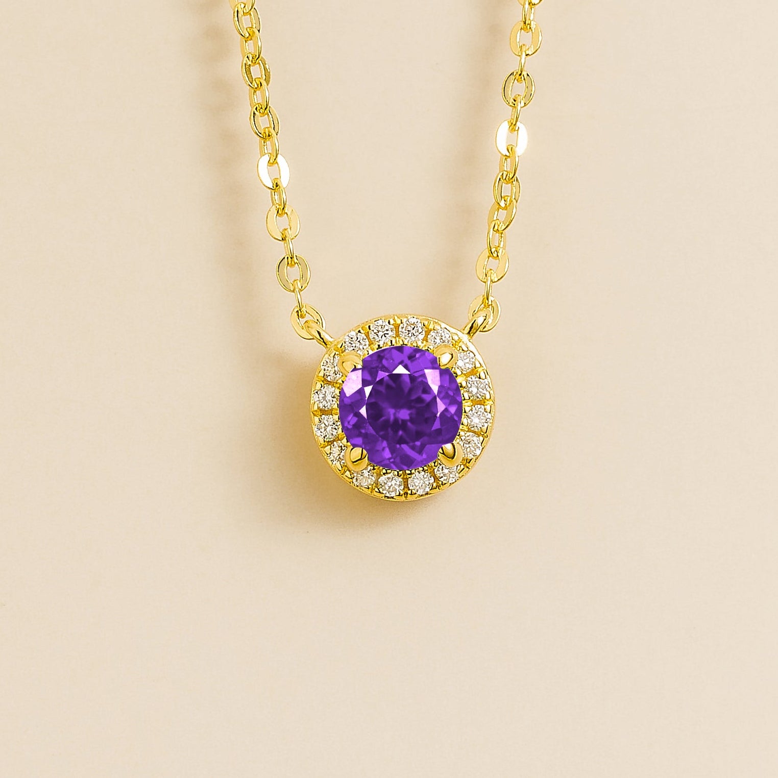 A gold necklace with a halo design featuring a round purple sapphire centerpiece surrounded by smaller diamonds, displayed against a light background.