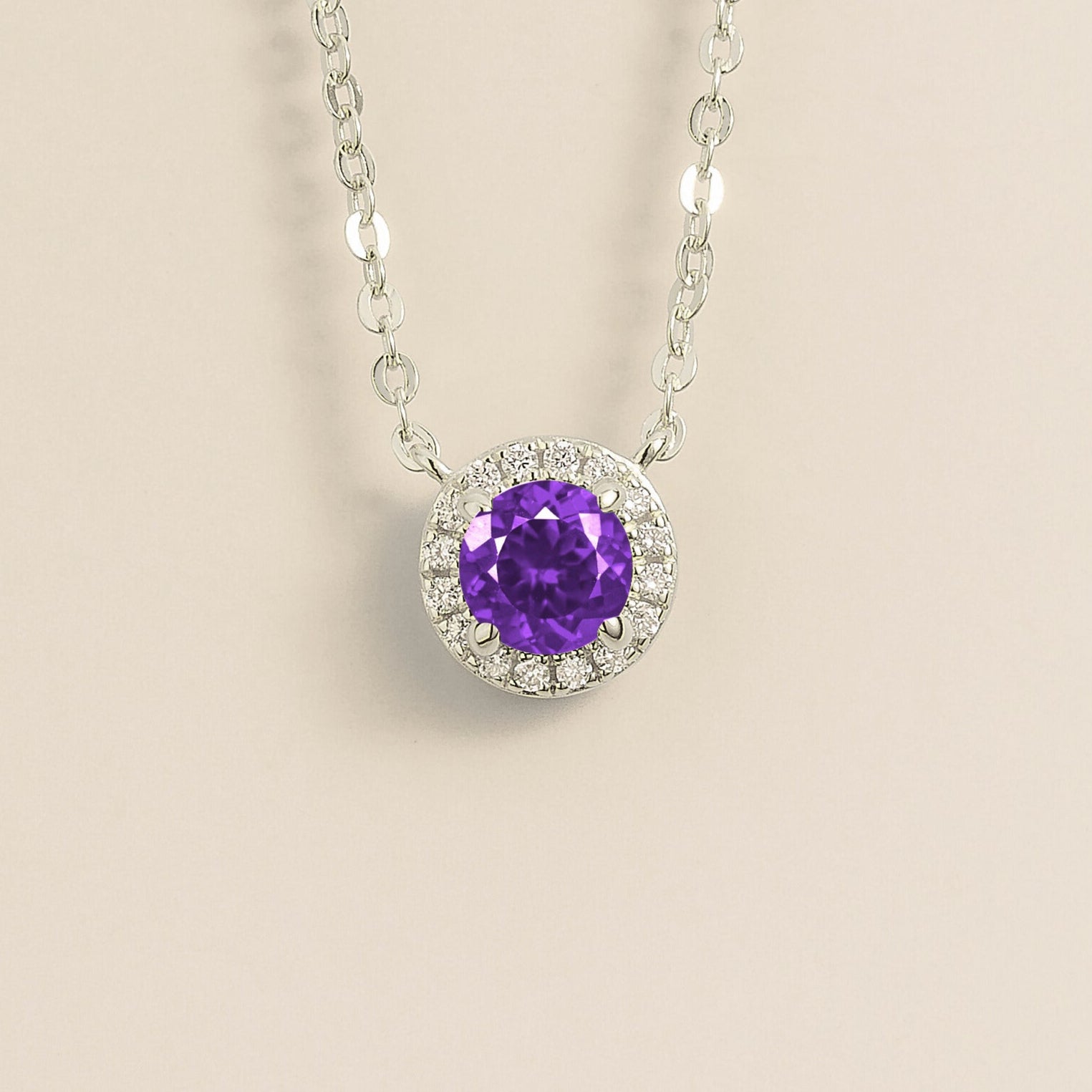 A white gold gold necklace with a halo design featuring a round purple sapphire centerpiece surrounded by smaller diamonds, displayed against a light background.