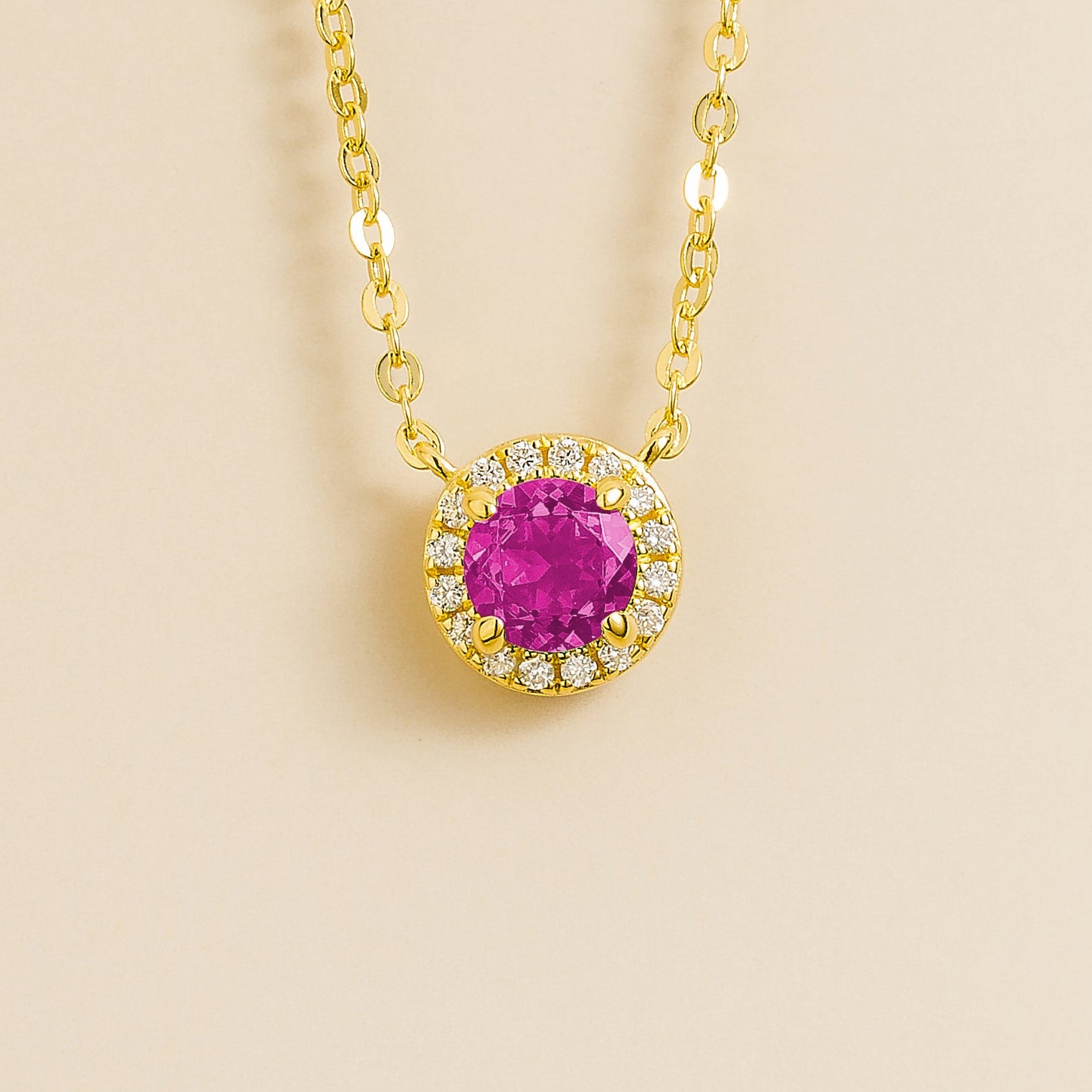 A gold necklace with a halo design featuring a round pink sapphire centerpiece surrounded by smaller diamonds, displayed against a light background.