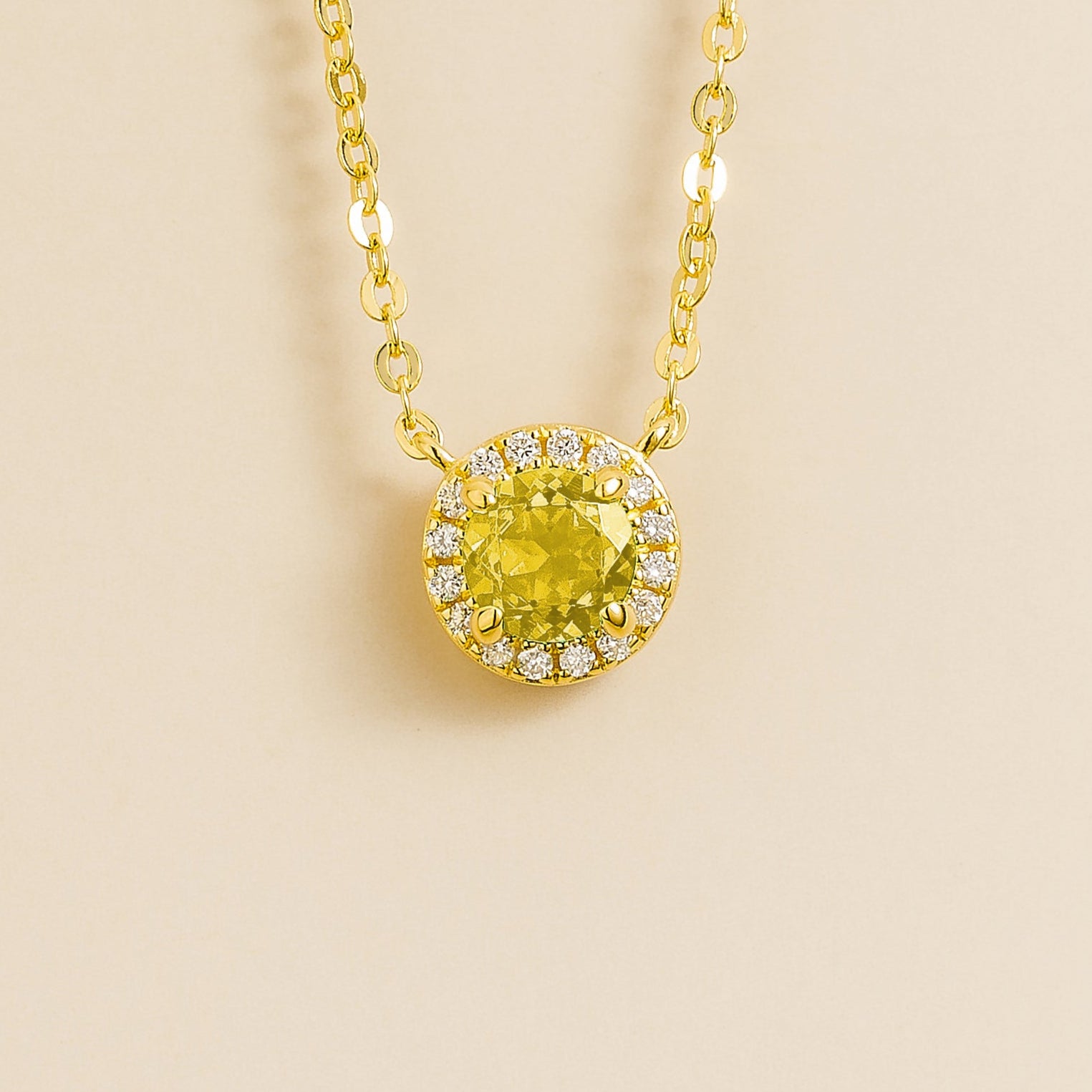 A gold necklace with a halo design featuring a round yellow sapphire centerpiece surrounded by smaller diamonds, displayed against a light background.