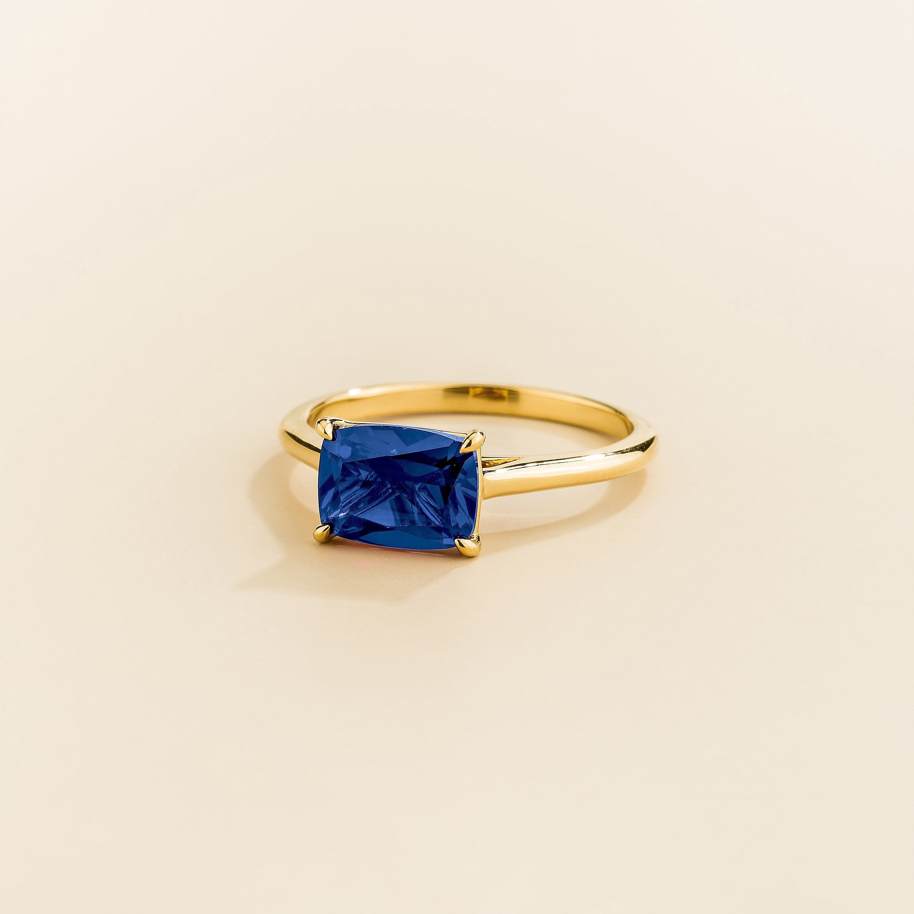 Juvetti yellow gold ring featuring a cushion-cut lab-grown blue sapphire in an east–west setting.