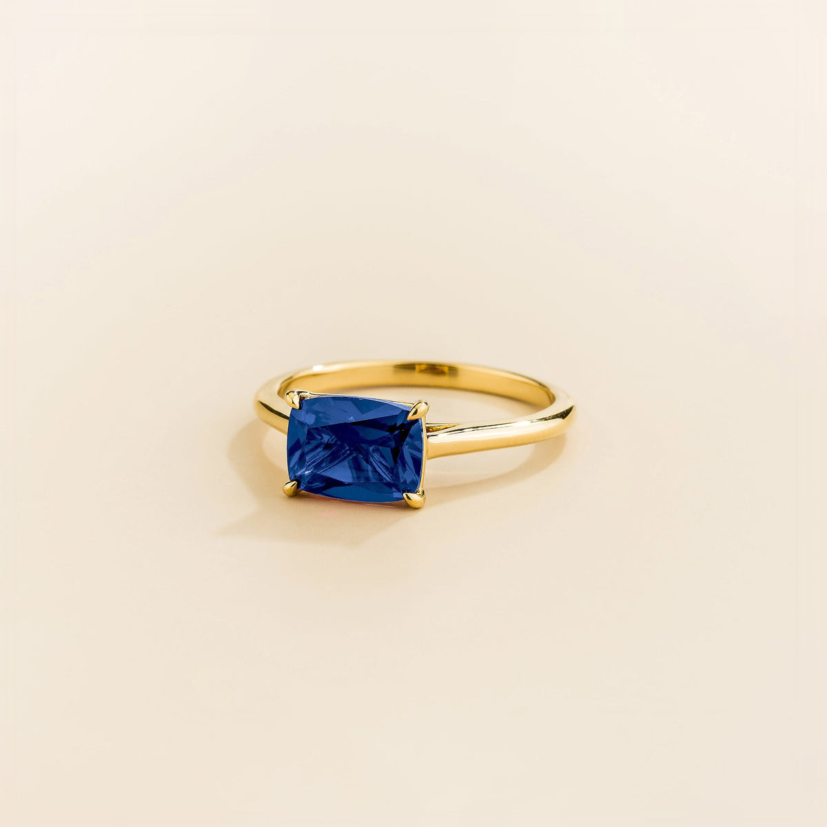 Juvetti yellow gold ring featuring a cushion-cut lab-grown blue sapphire in an east–west setting.