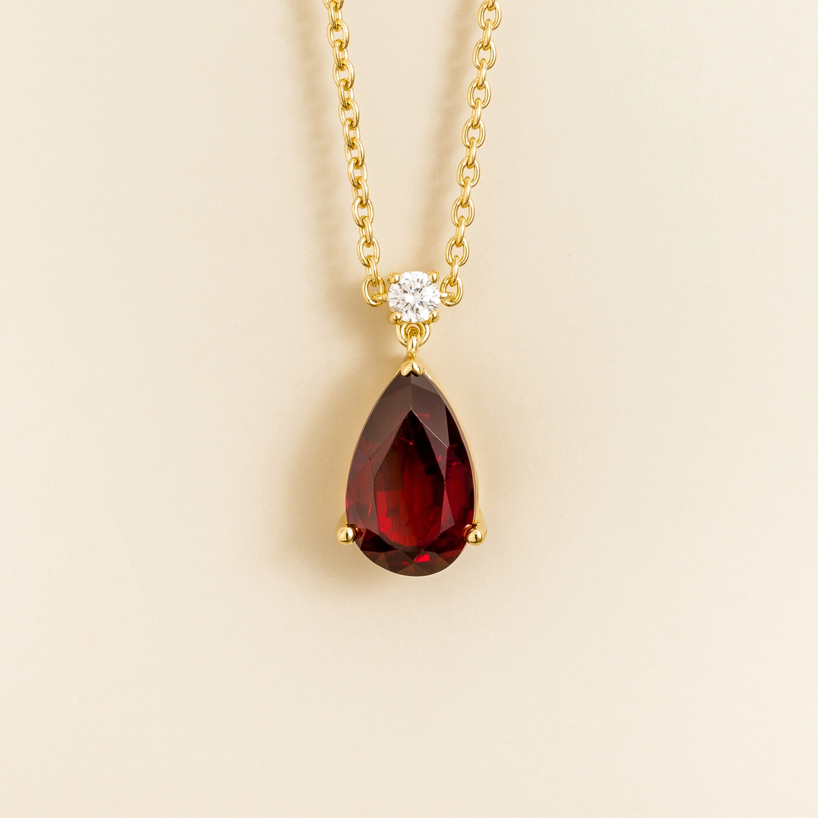Classic gold necklace with a teardrop pear shape pigeon blood red ruby gemstone pendant with round diamond on a beige background