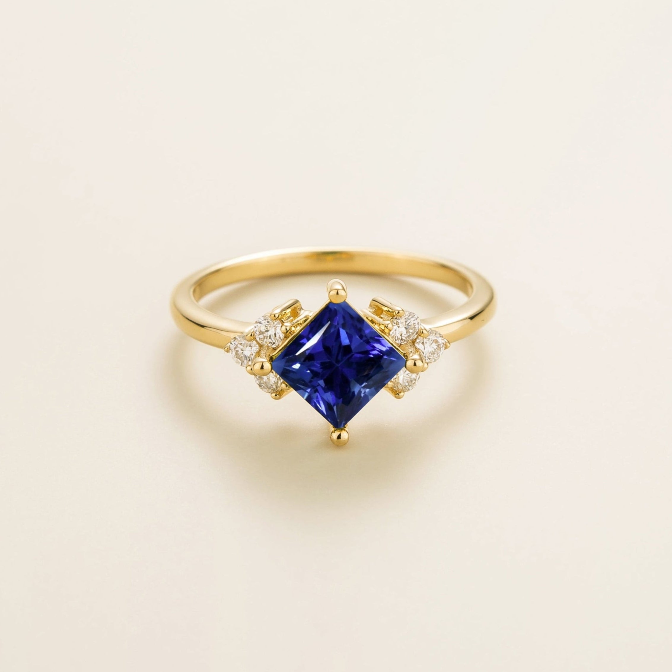 A gold ring with a princess-cut royal blue sapphire center stone and smaller diamond accents on the band.