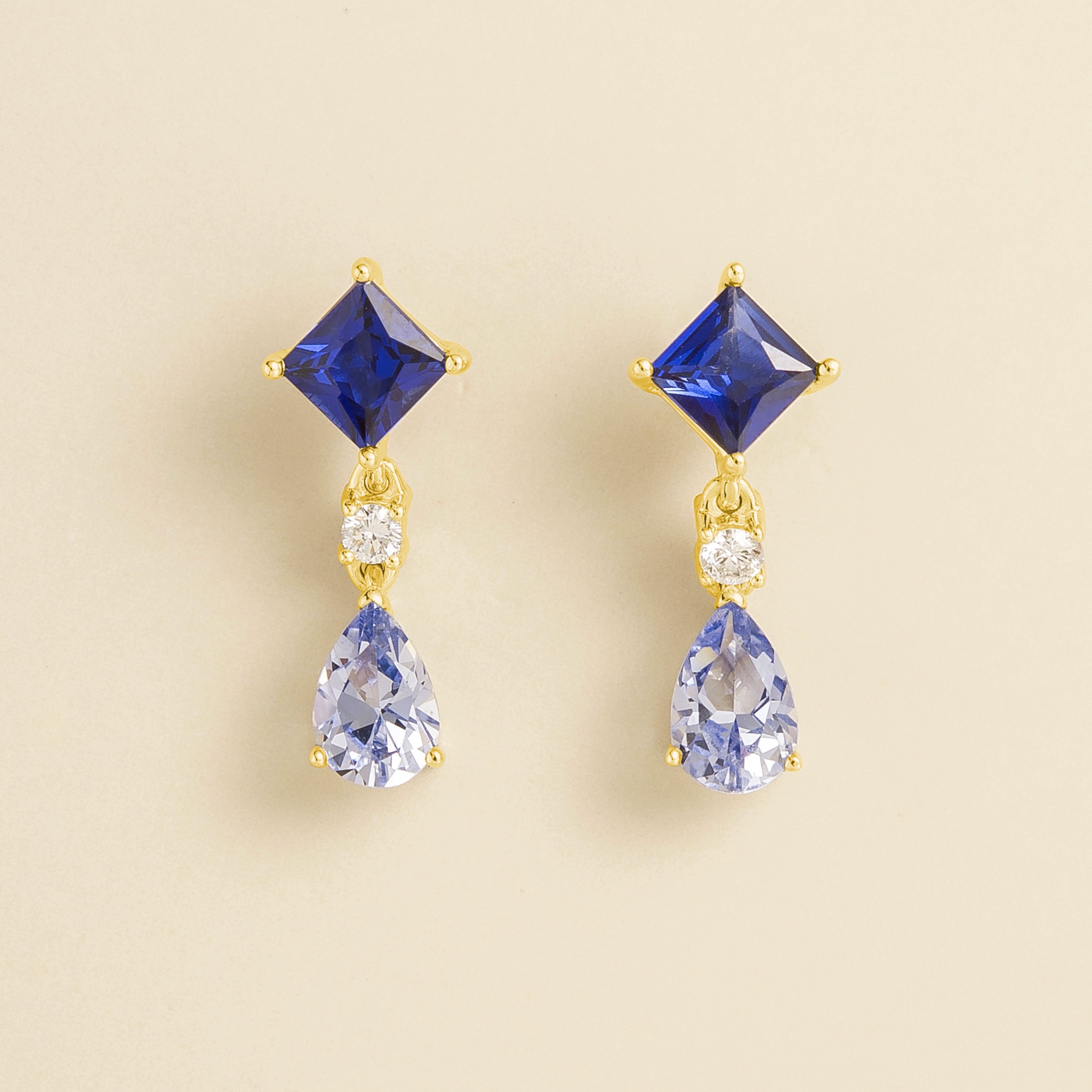 Pair of drop earrings with pear shape and princess shape blue sapphire gemstones, with round diamond accent sent in gold