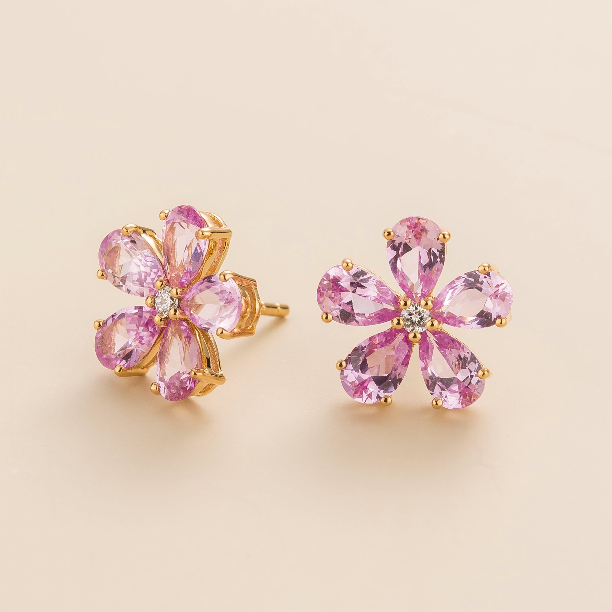A pair of gold earrings featuring pink sapphire flowers and smaller diamonds, set in yellow gold.
