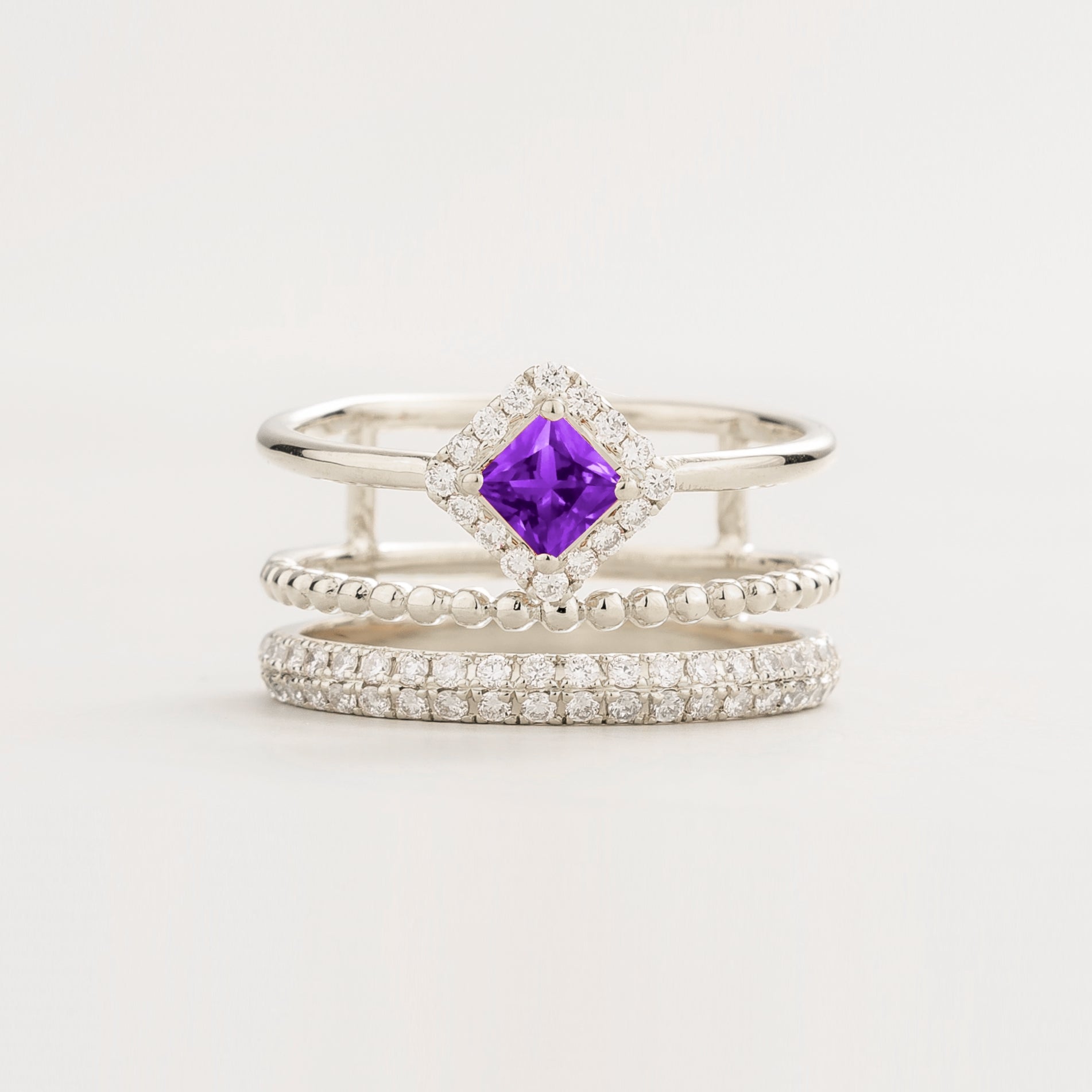 Set of three stacking white gold rings with a princess cut purple gemstone and round diamonds pavƩ
