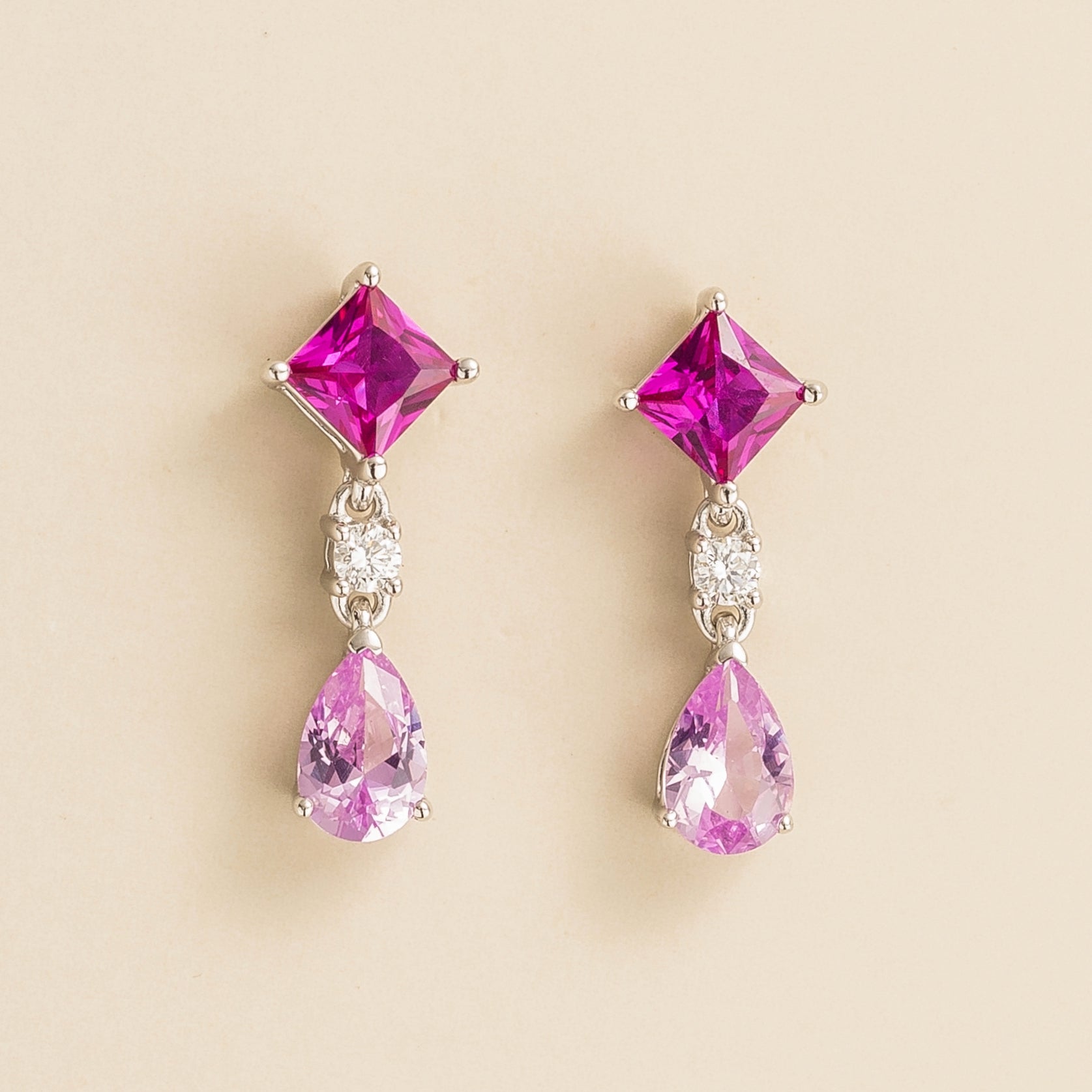 A pair of white gold earrings featuring pink sapphire and diamond accents, with the earrings positioned against a neutral background.