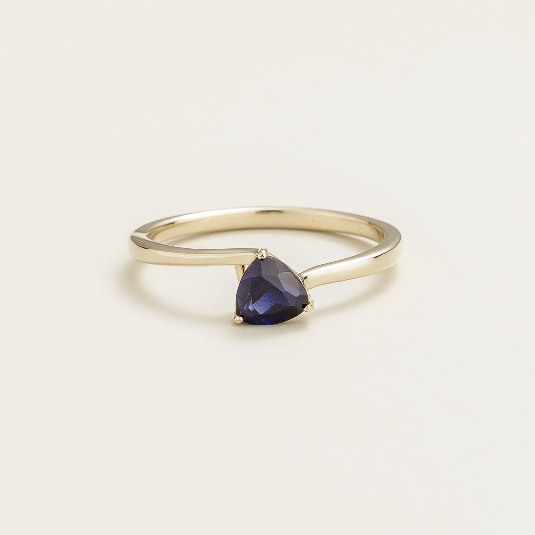 A solitaire white gold ring with a trillion-cut blue sapphire in a curved modern setting on a plain background.