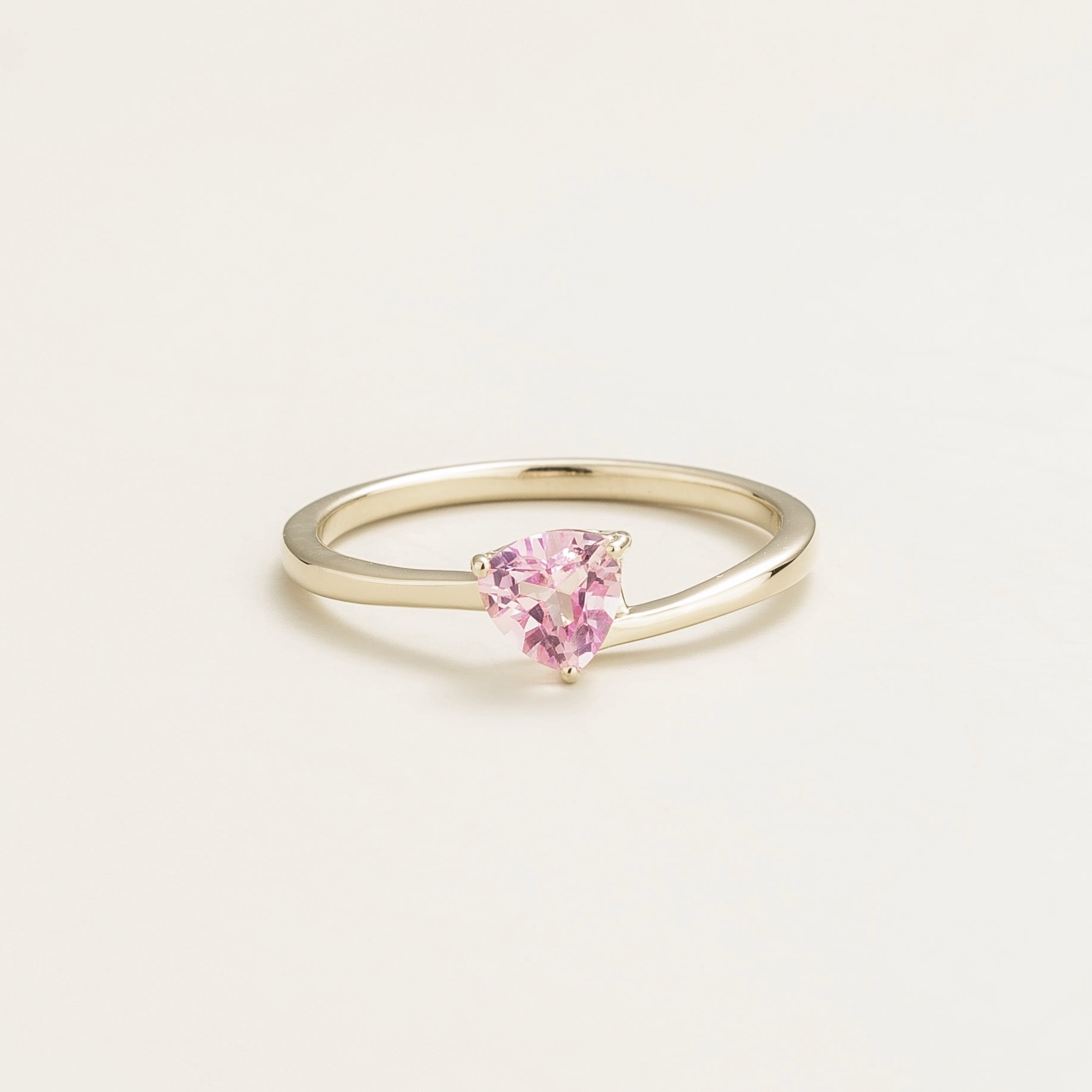A white gold solitaire ring with a trillion-cut pink sapphire in a curved setting on a plain background.