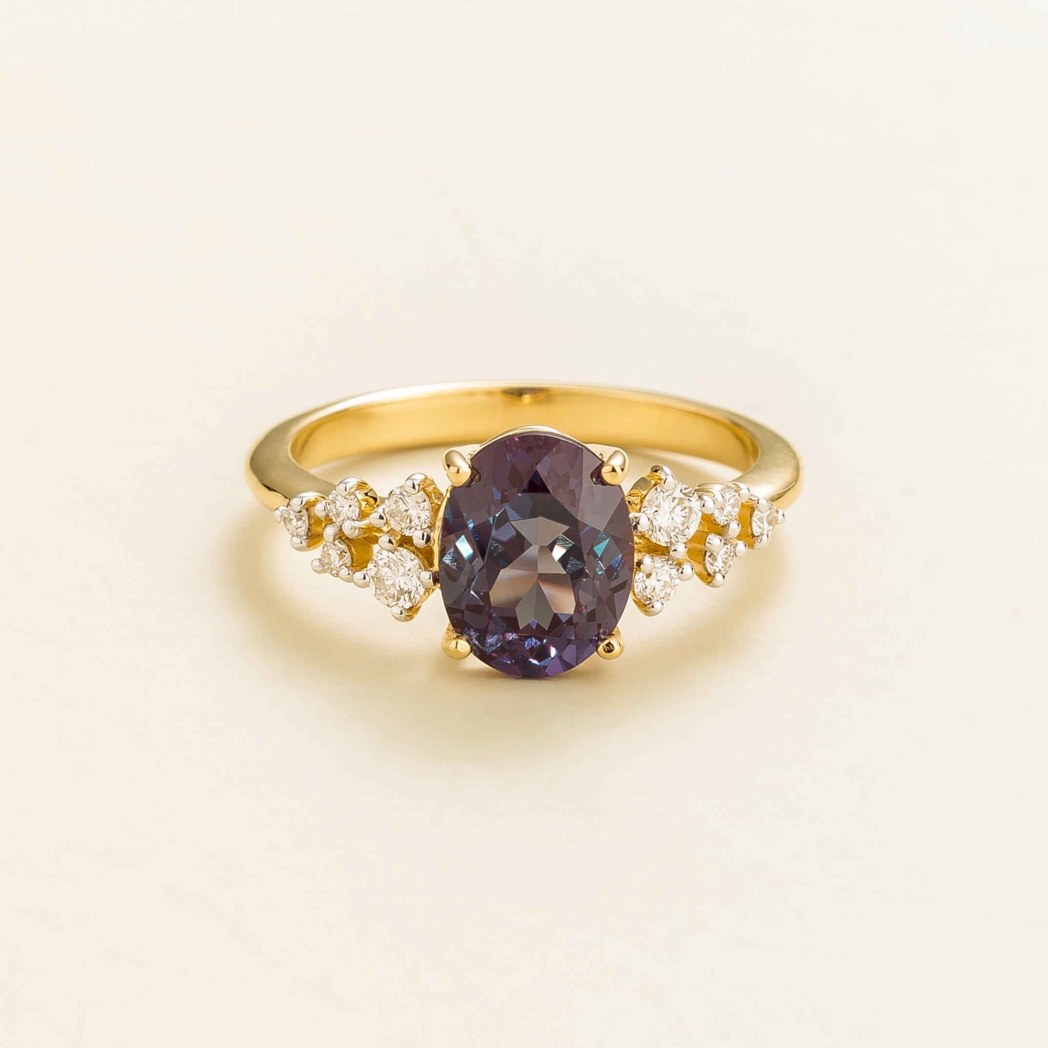 A gold ring with a central oval alexandrite gemstone and smaller diamonds cluster.