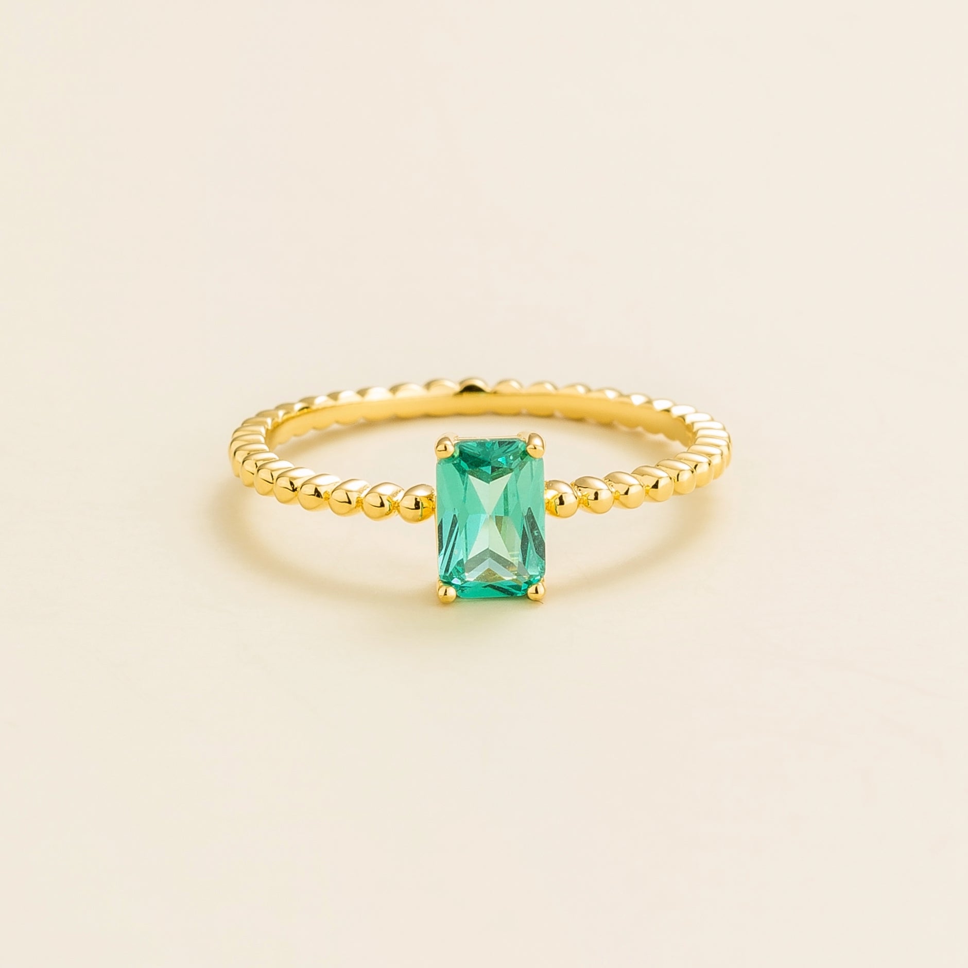 Juvetti gold ring featuring an emerald-cut lab-grown paraiba gemstne on a beaded band.