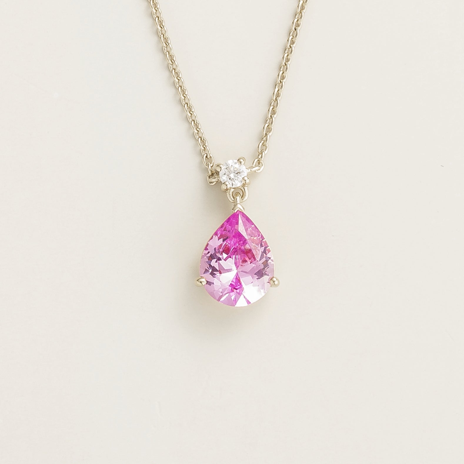 A white gold necklace with a medium-sized pear shape pink sapphire pendant and a smaller round diamond, displayed against a neutral background.