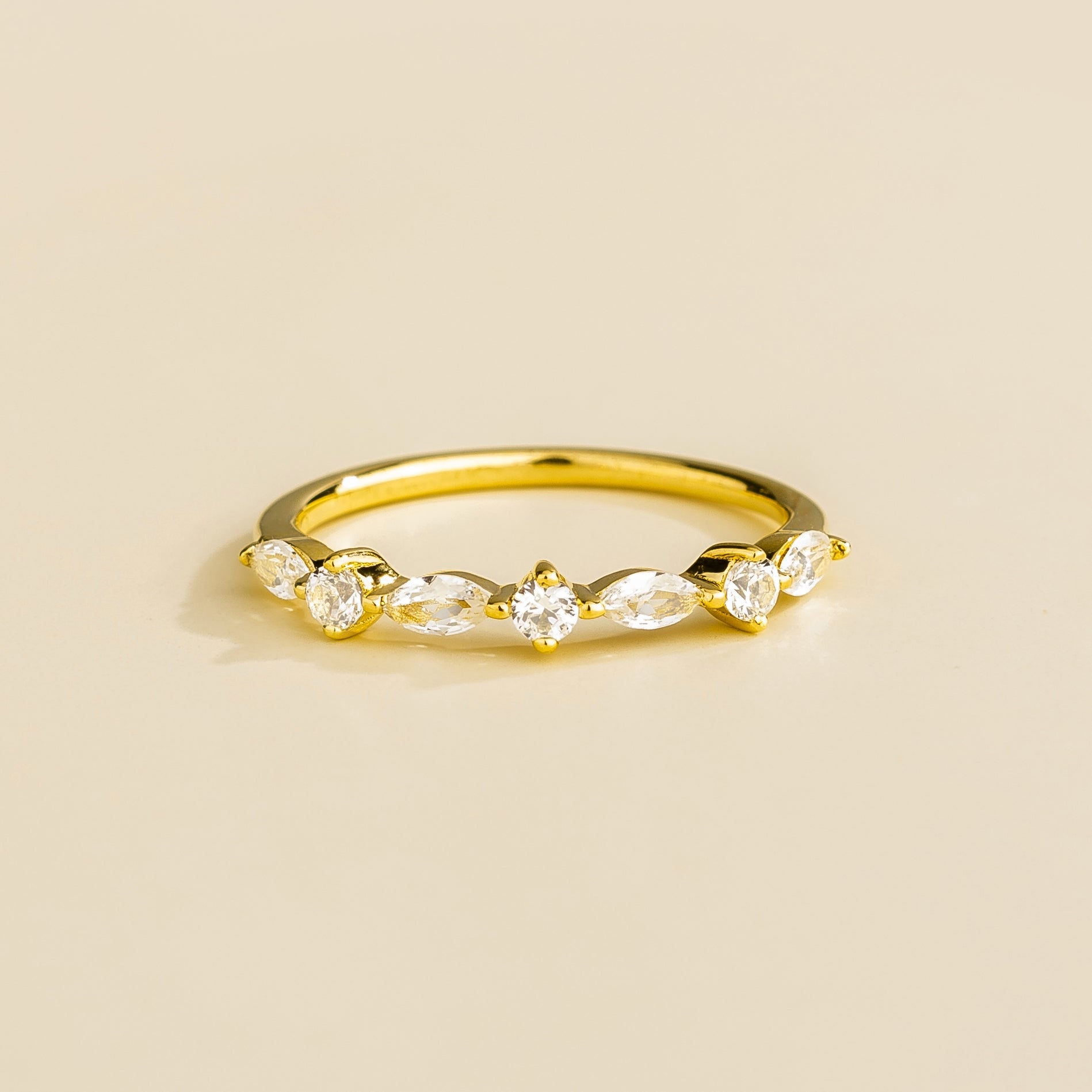 A gold band ring with marquise and round cut diamonds set in an alternating pattern on a plain background.