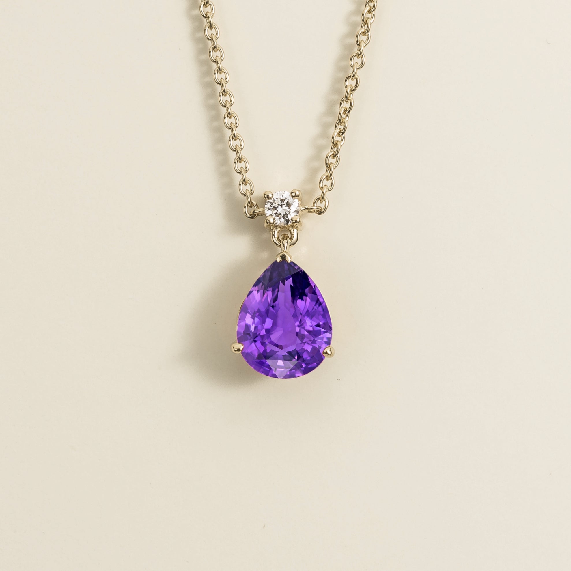 A classic pendant necklace with a pear shape purple sapphire and round diamond set in white gold, displayed against a neutral background.