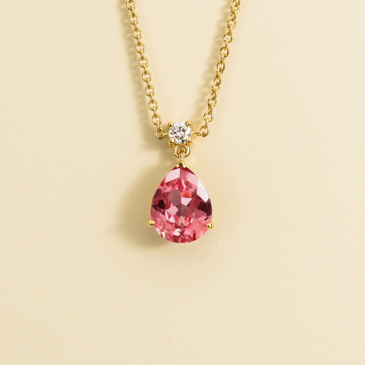 A classic pendant necklace with a pear shape padparadscha sapphire and round diamond set in gold, displayed against a neutral background.