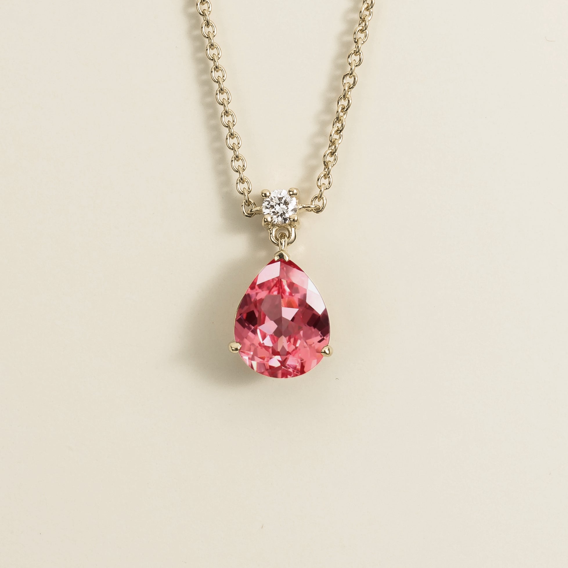 A white gold necklace with a medium-sized pendant featuring a pear shape Padparadscha sapphire and a smaller diamond, displayed against a plain background.