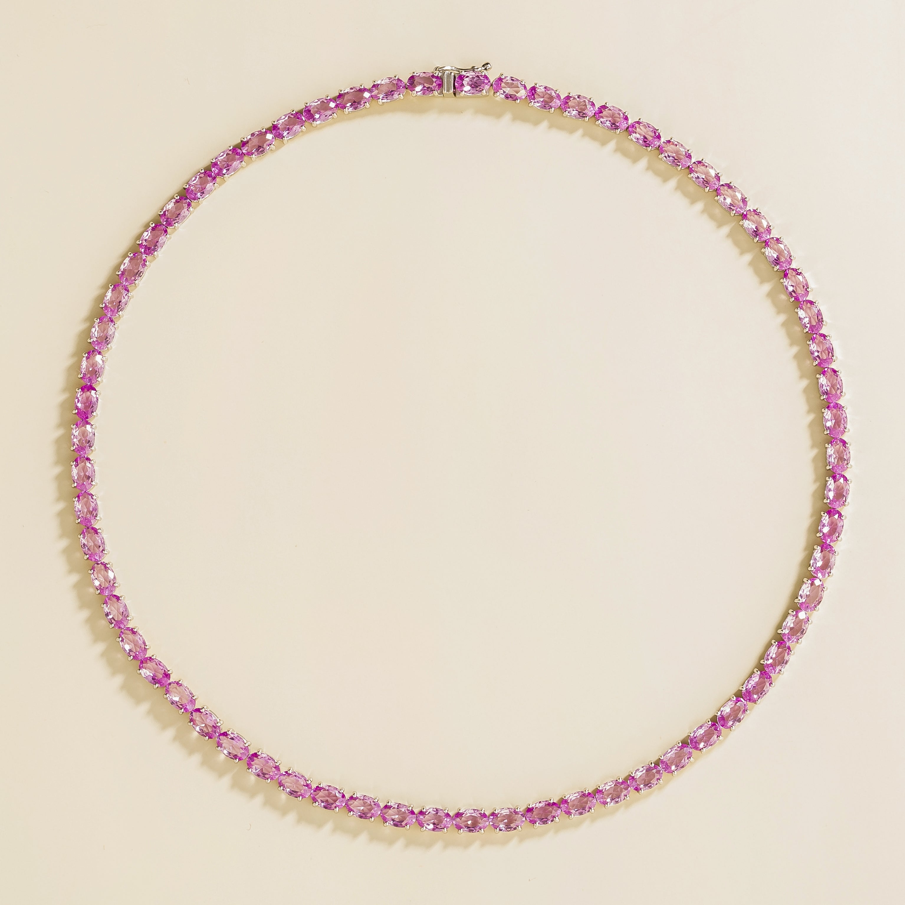 A white gold tennis necklace set with pink sapphire gemstones.