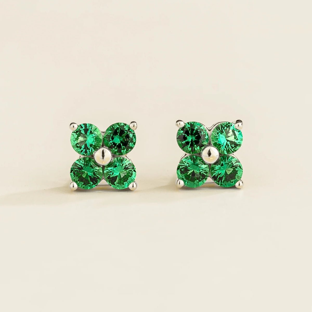 A pair of white gold stud earrings set with emeralds, featuring a 4-gemstone clover design.