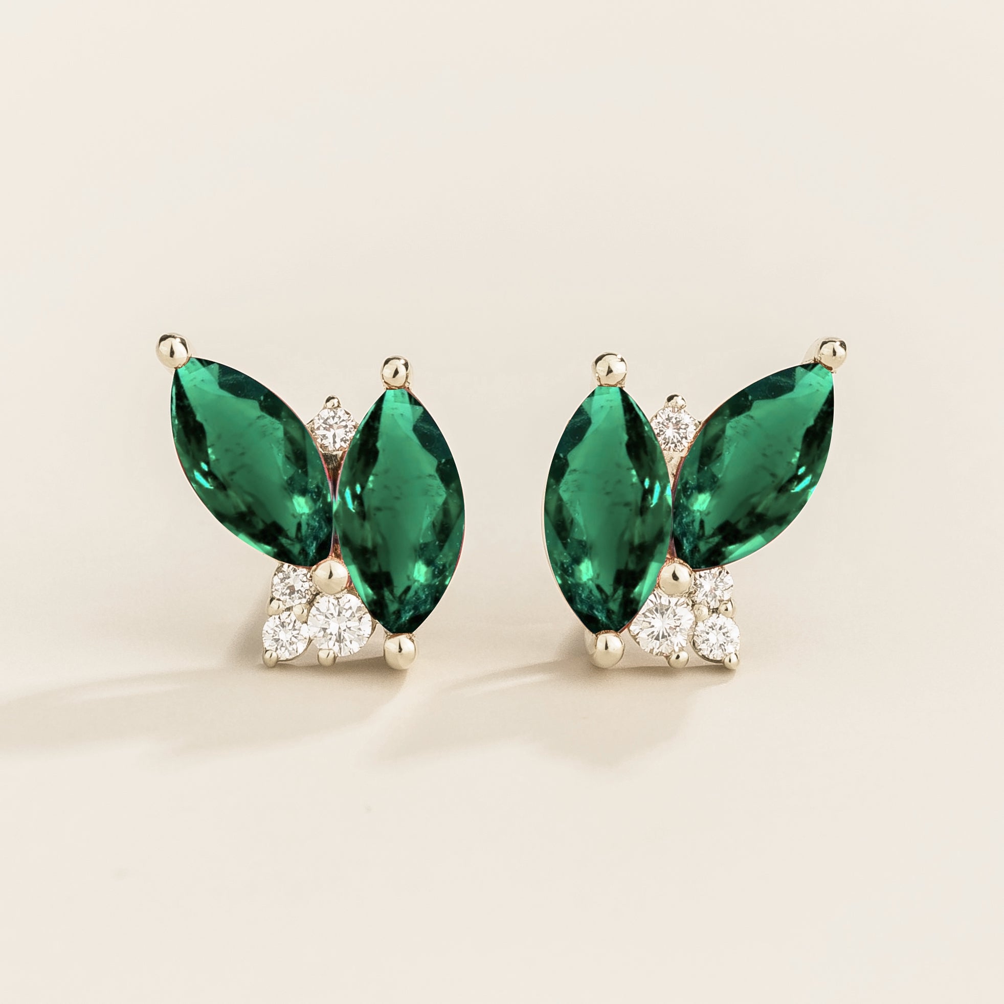 A pair of Vento white gold earrings featuring marquis emeralds and round diamonds, with a butterfly-like shape and a white gold setting.