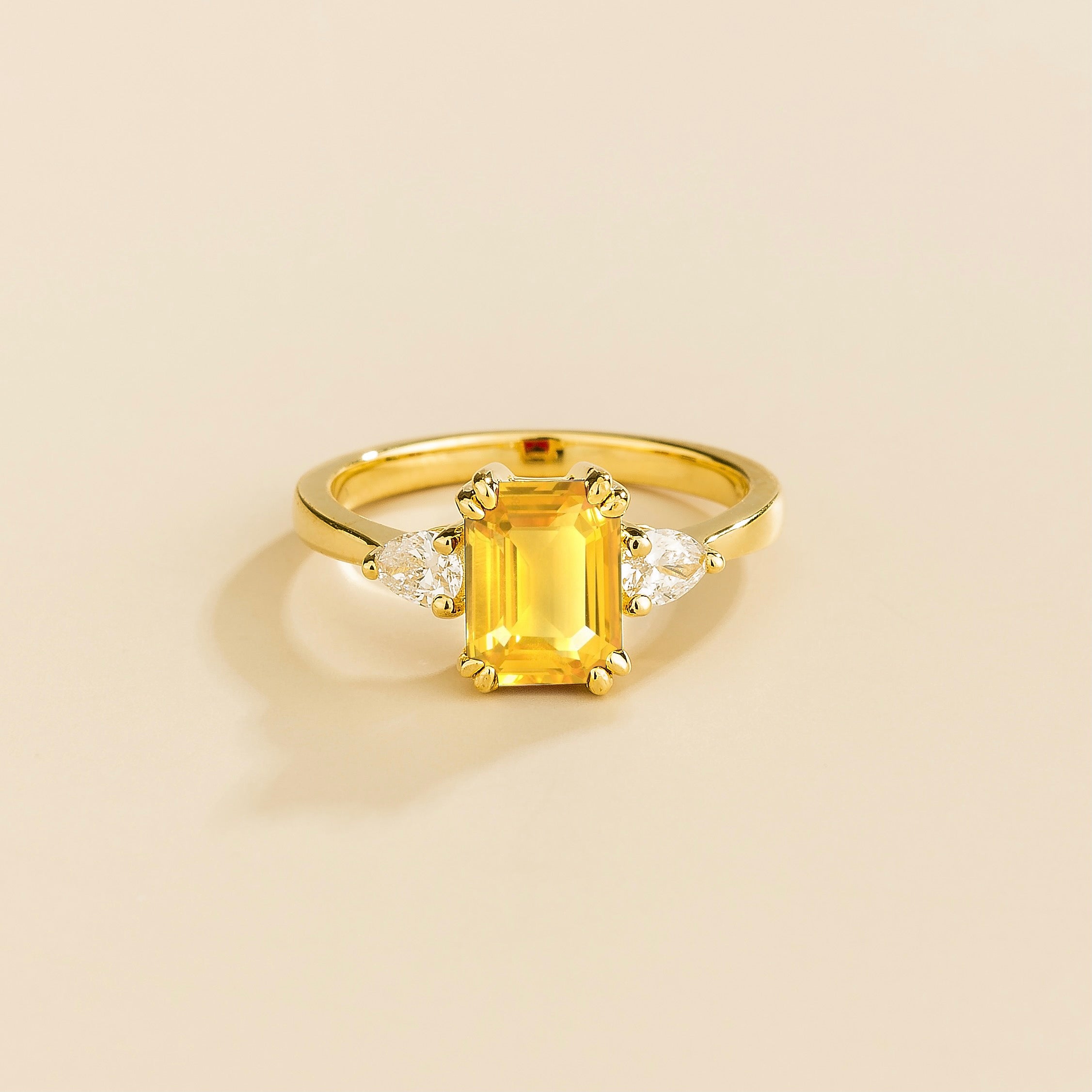 A gold ring with a yellow sapphire center stone and pear shape diamonds set in yellow gold, emerald/octagon cut for the sapphire.
