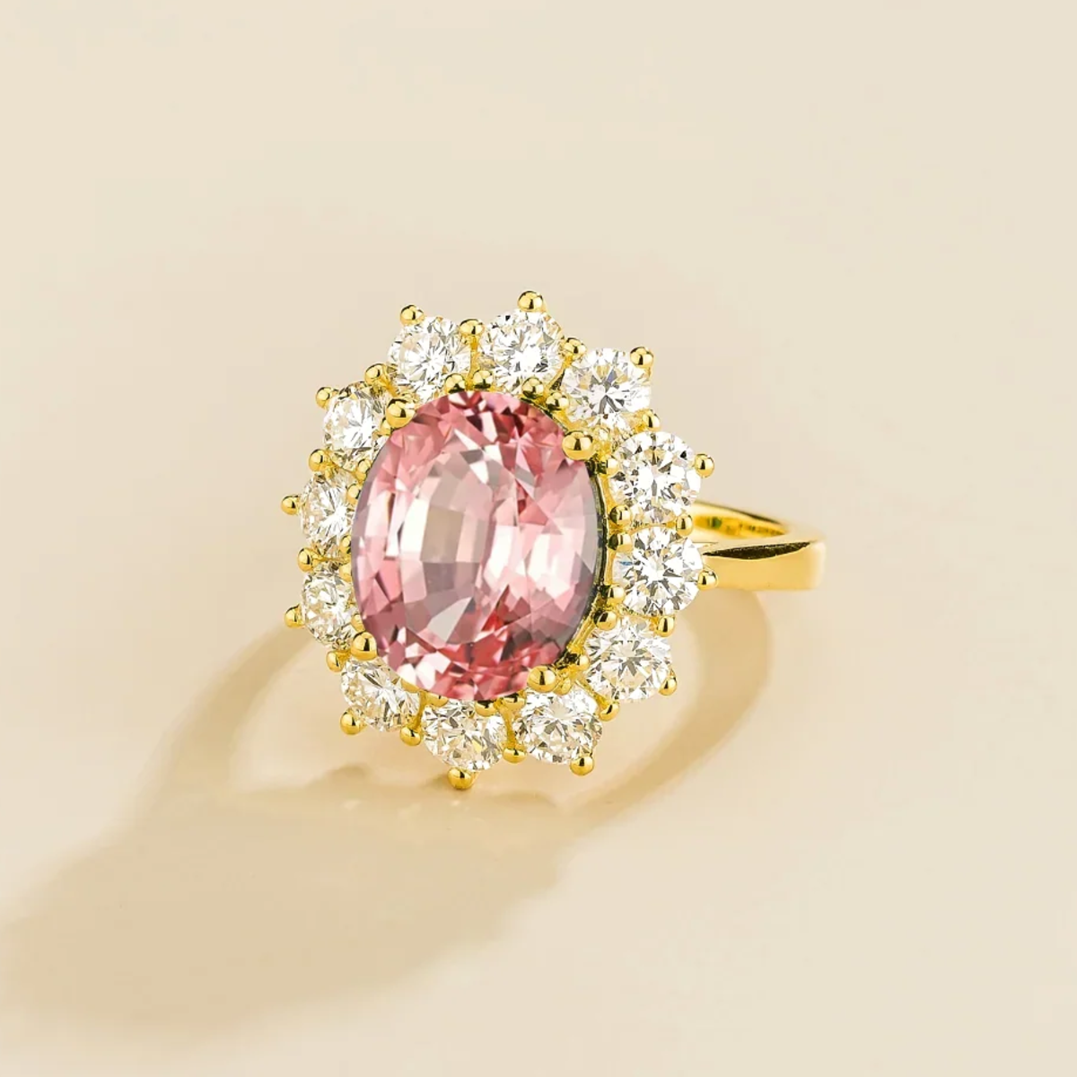 Gold ring with a padparadscha gemstone and diamond halo accents on a beige background