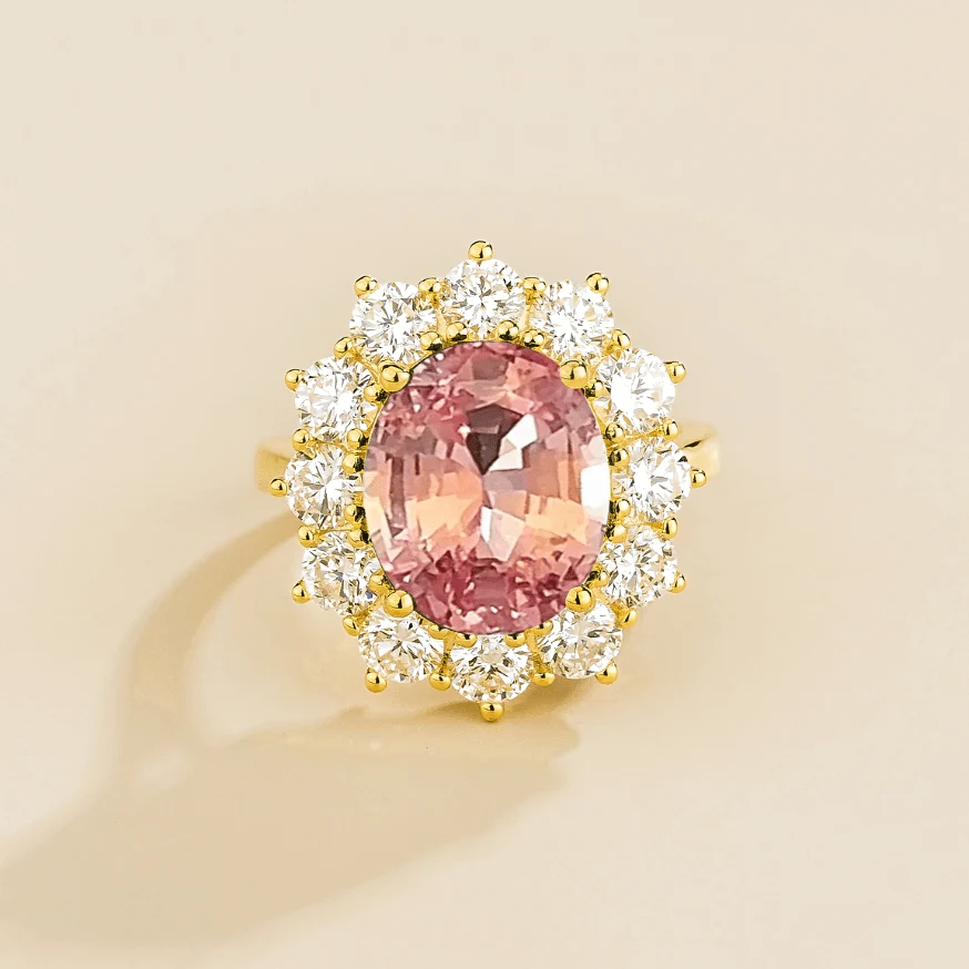 Juvetti yellow gold halo ring featuring an oval lab-grown padparadscha sapphire surrounded by round lab-grown diamonds.