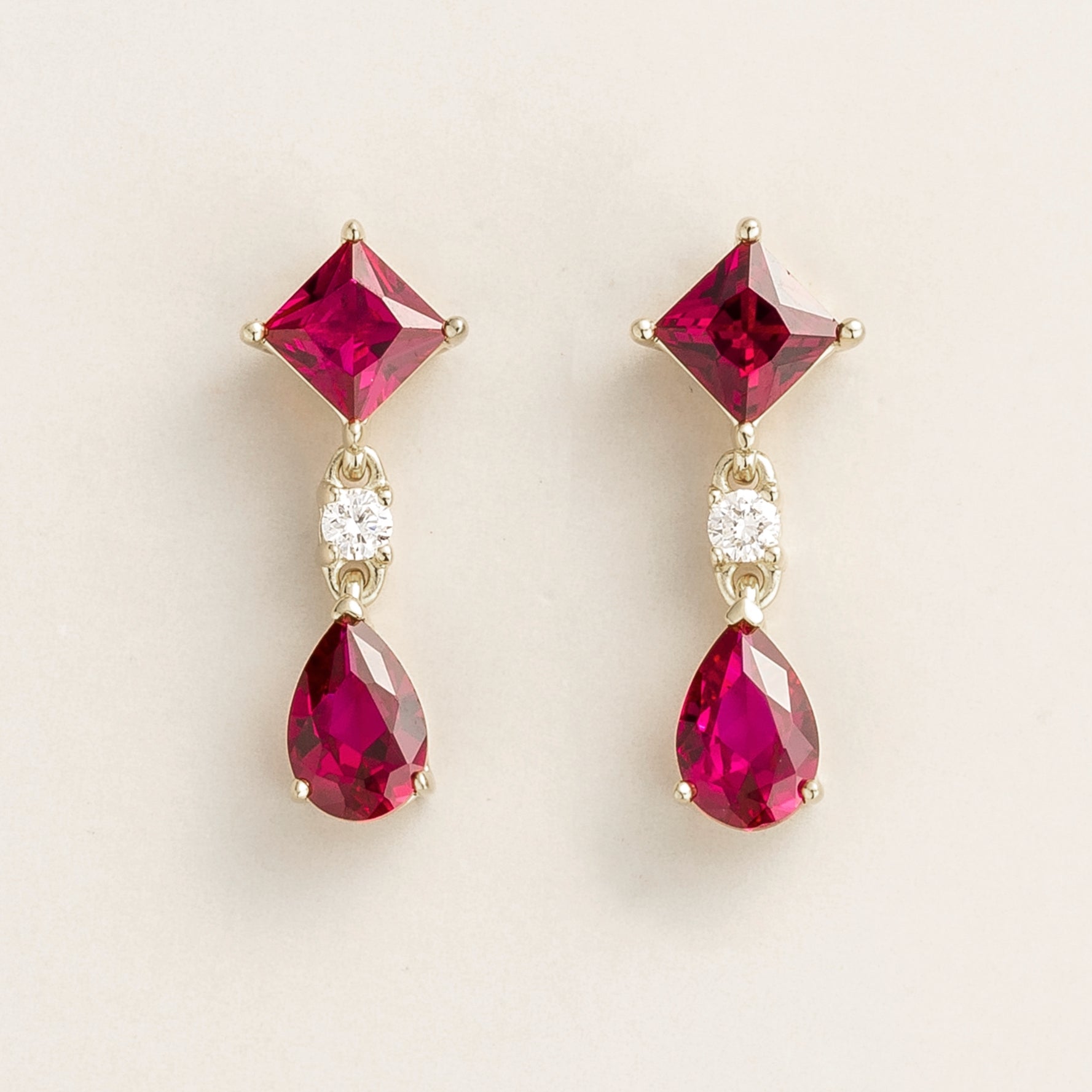 A pair of white gold earrings with one square-cut ruby and one pear-cut ruby alternately set with round-cut diamonds.