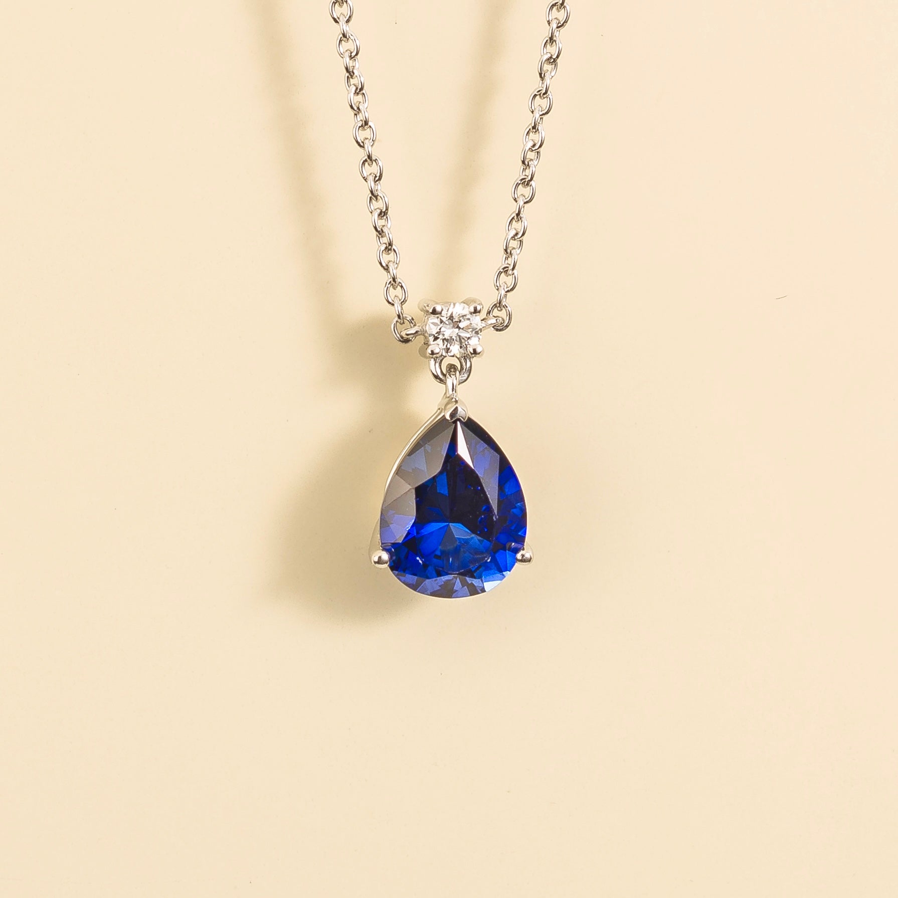 A classic pendant necklace with a pear shape blue sapphire and round diamond set in white gold, displayed against a neutral background.